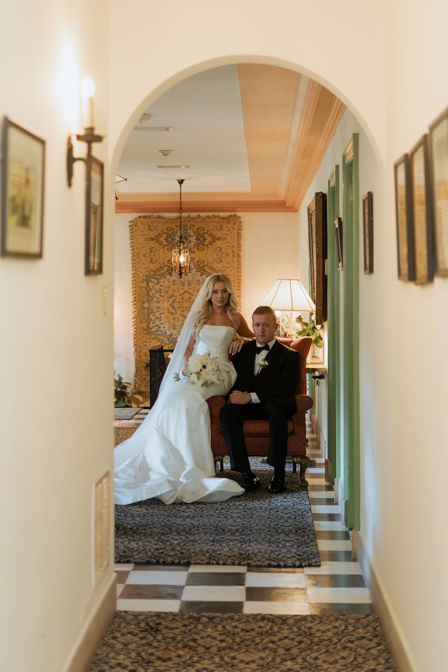 Elegant hallway with arched doorways and patterned carpet showcases wedding party in multiple reflective mirrors.