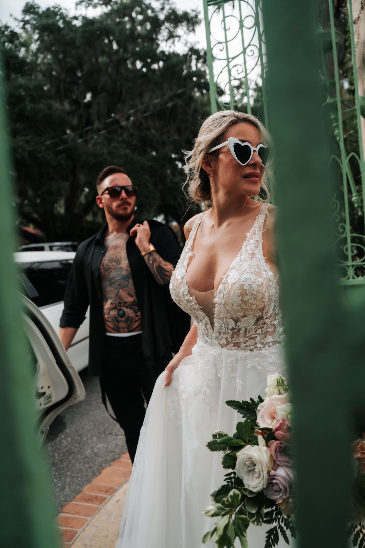 A couple in wedding attire share a joyful moment together through green iron gates in an outdoor setting.