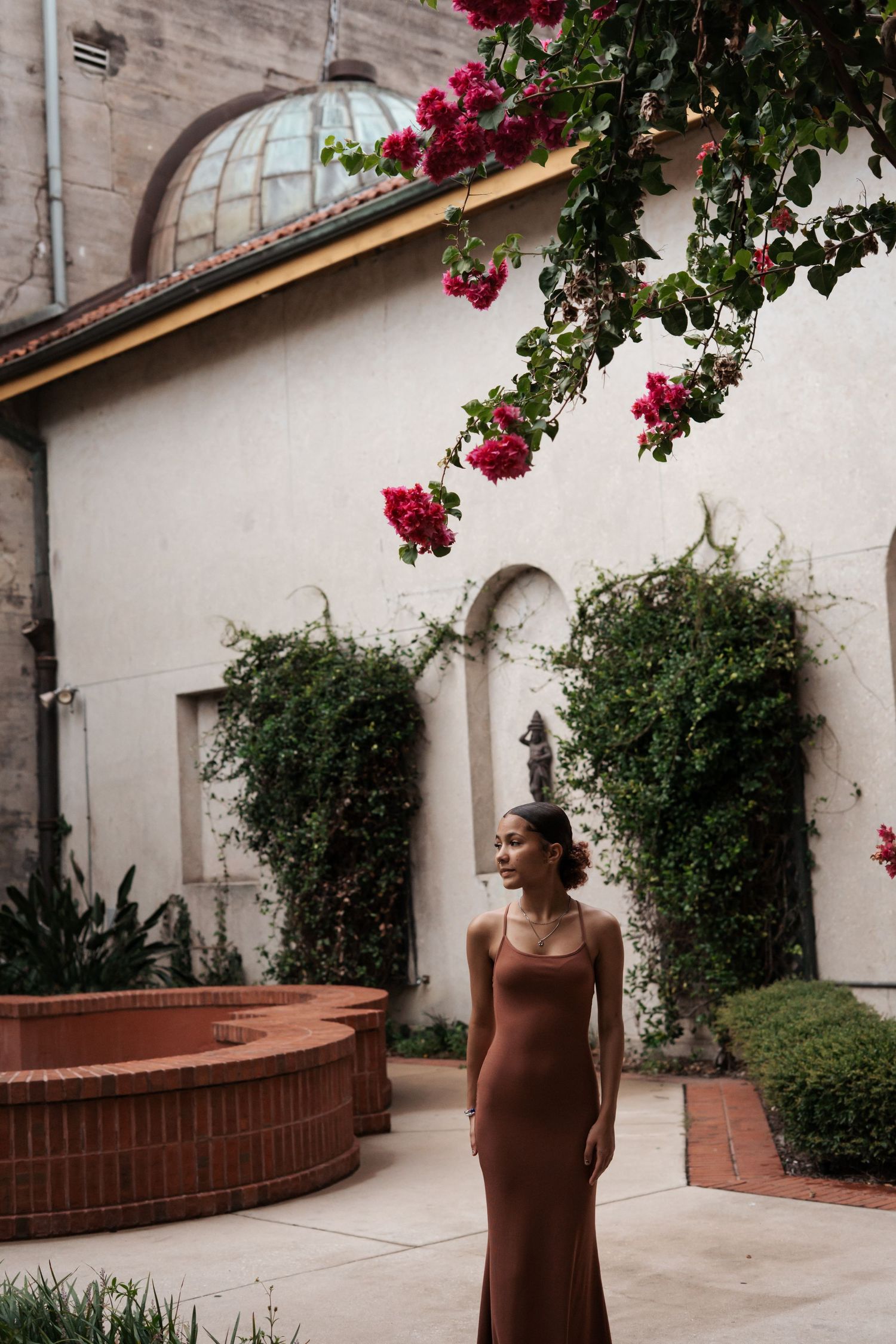 Elegant brown dress photographed in a courtyard with climbing bougainvillea and architectural details at the Lightener Museum