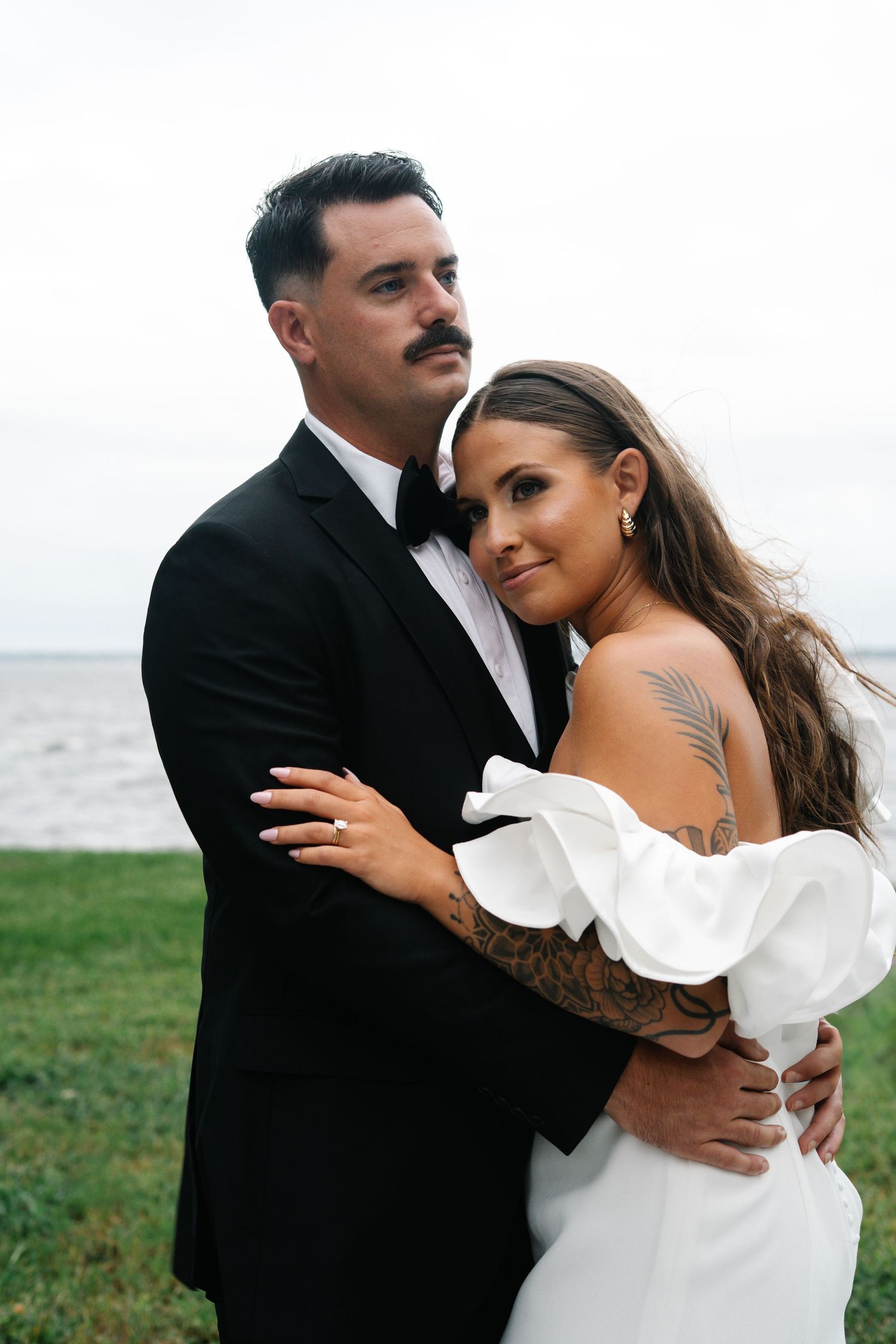 A romantic couple embraces on a cloudy day by the water in a series of intimate wedding photos.