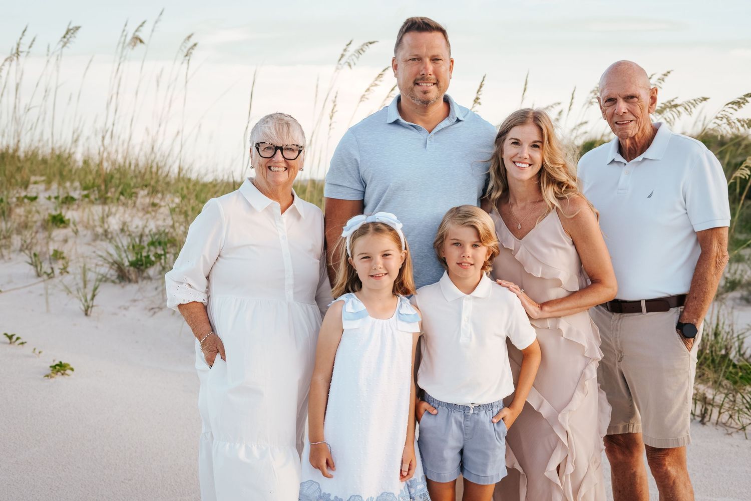 A group poses together on a sandy beach wearing coordinated blue and white casual summer outfits.