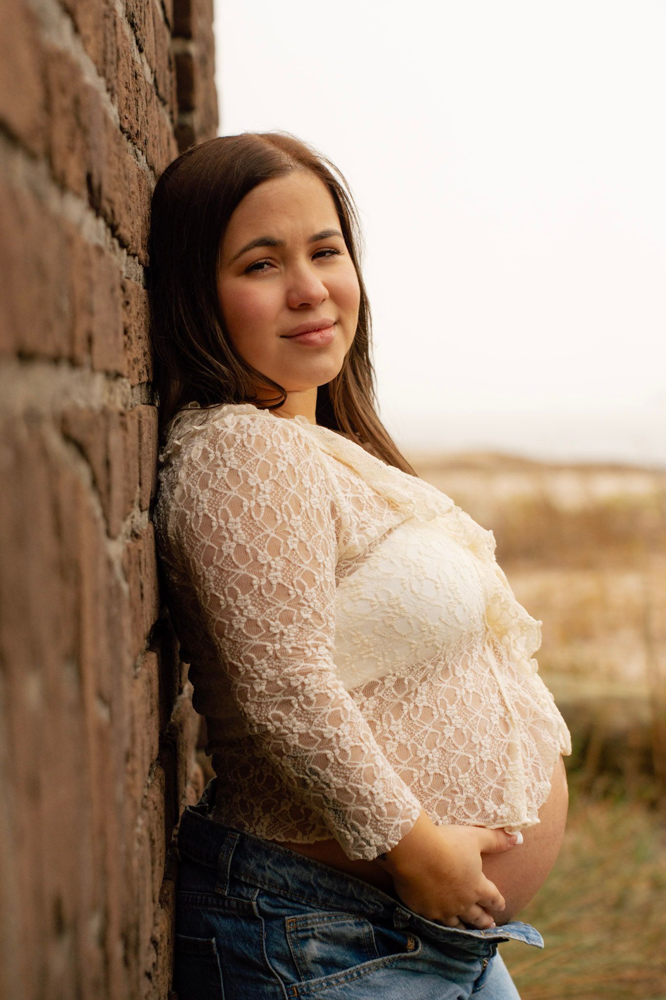 Portrait of someone wearing a delicate white lace top against a rustic brick wall background at sunset.