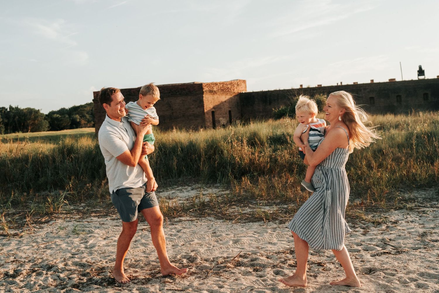 Two couples enjoying a playful moment together at sunset on a sandy beach near an old stone fortress.