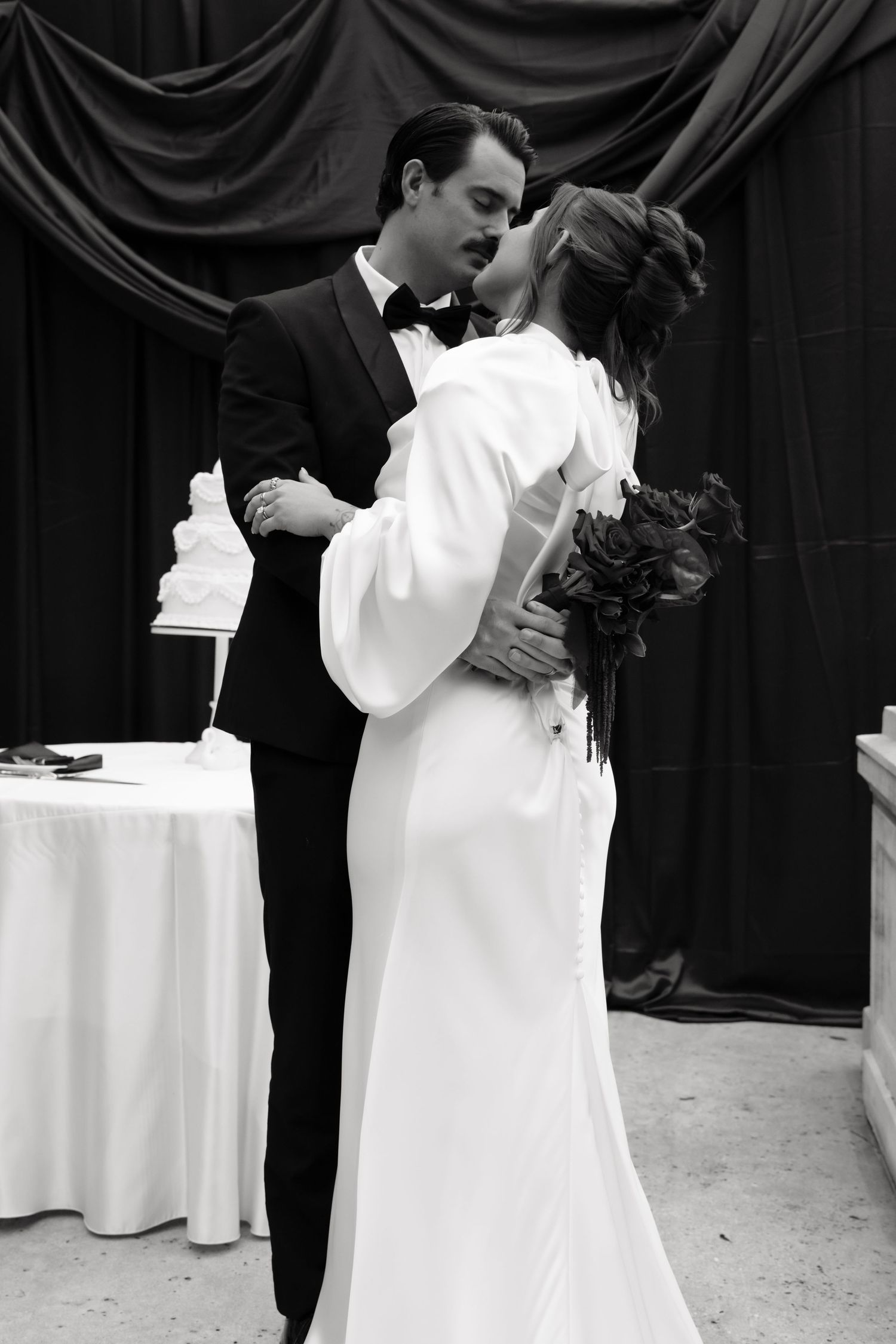 Black and white wedding photo series showing intimate moments between newlyweds against dark backdrop.