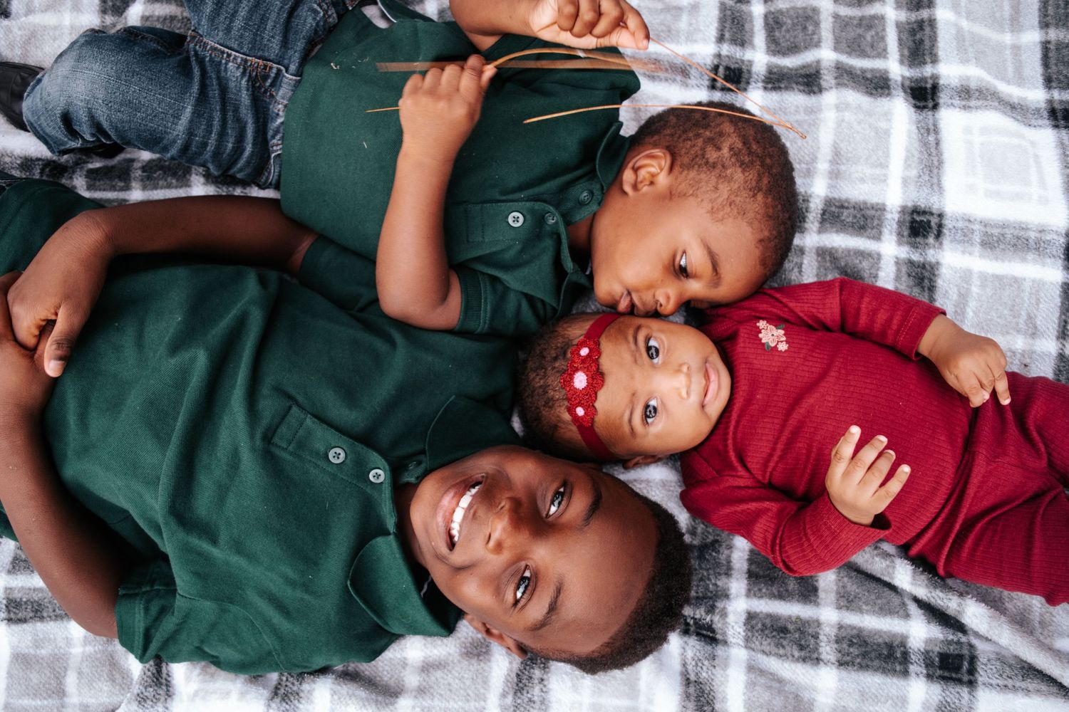 Family members share playful moment while laying on blanket outdoors.