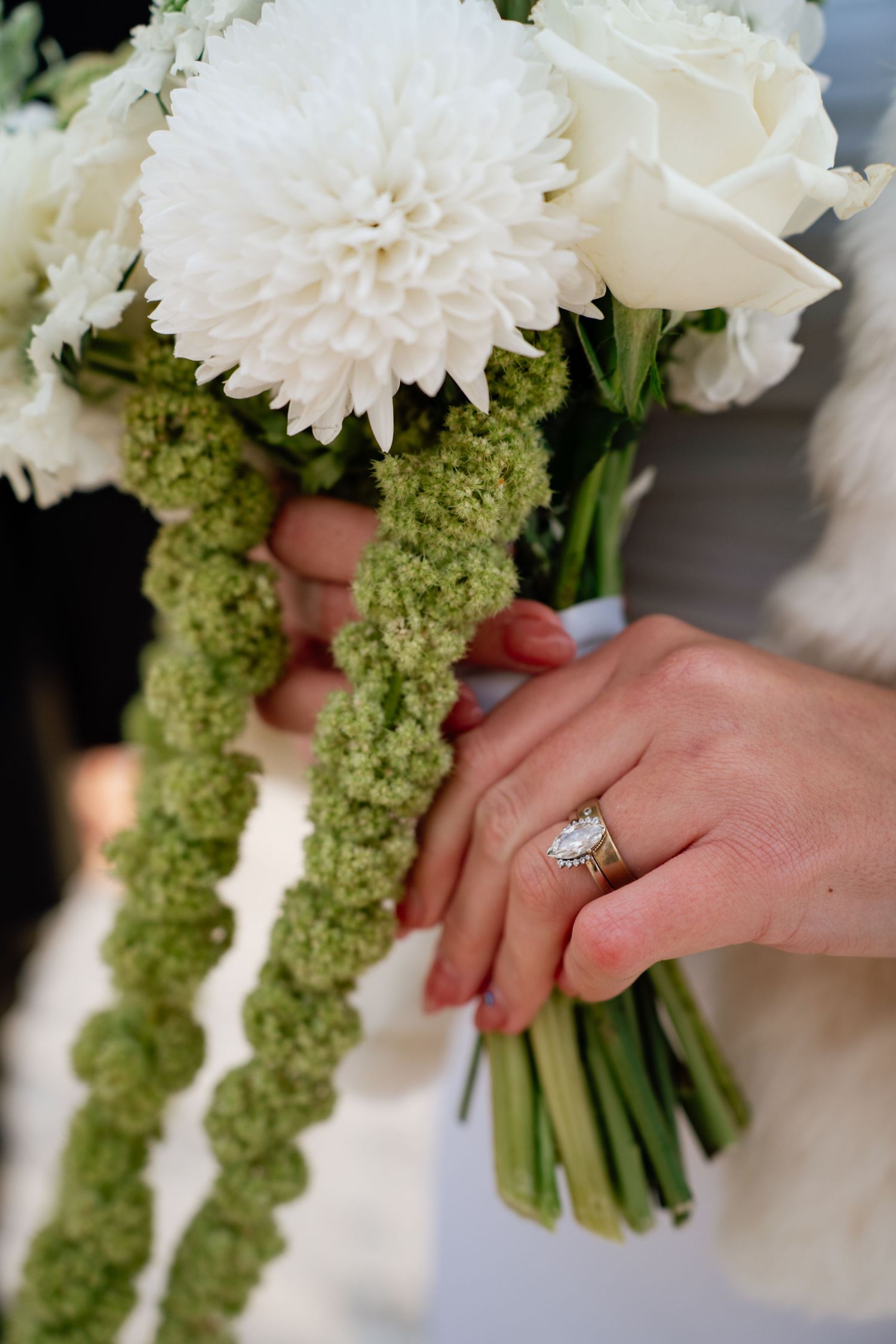 A wedding bouquet with white chrysanthemums and green amaranthus is held, showing an engagement ring detail.