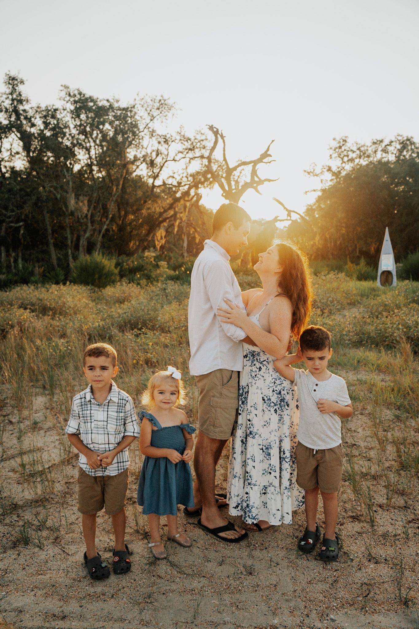 Family portrait at sunset with golden light filtering through bare tree branches.