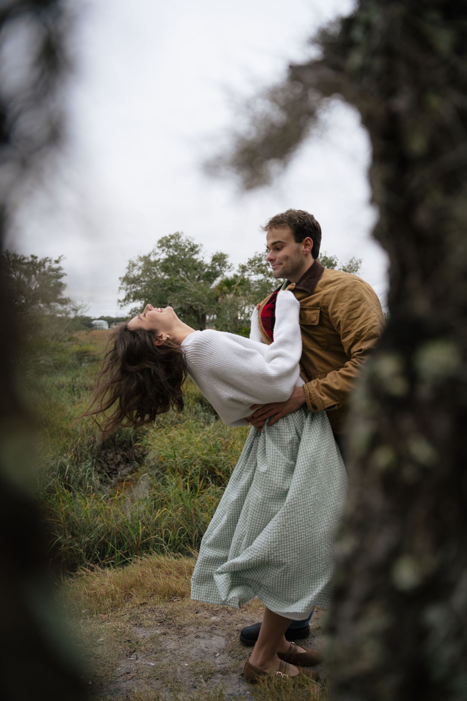 A couple dances together in a field, with the person in white being dipped dramatically by their partner in brown.