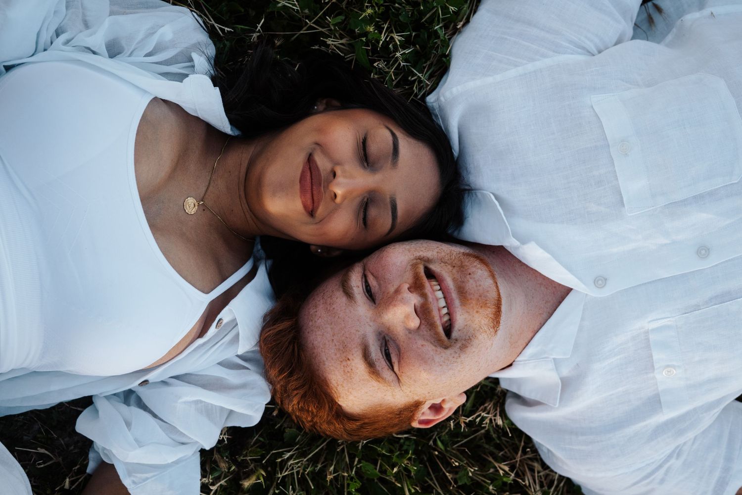 Two people in white shirts lying on grass with closed eyes and content smiles.