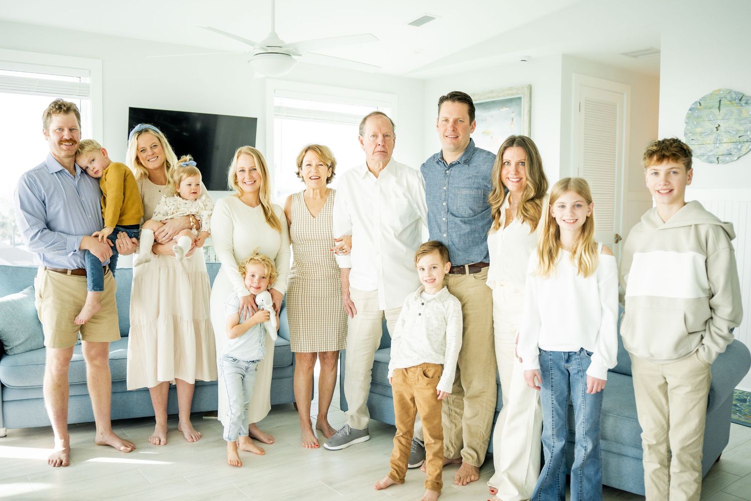 Large family group posing together for an indoor portrait in coordinated light-colored outfits.