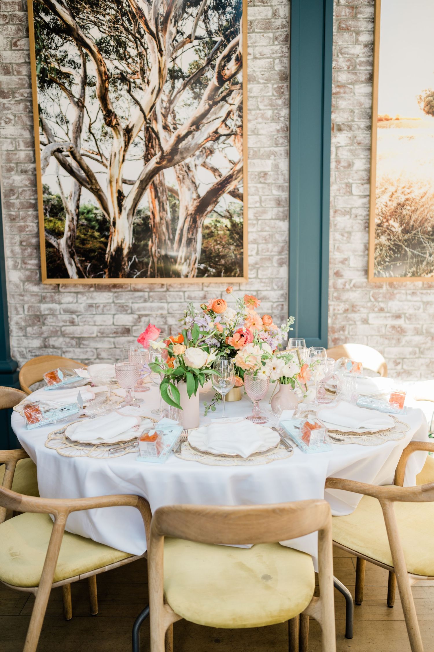 Elegant table setting with floral centerpiece and large tree artwork in modern dining room.