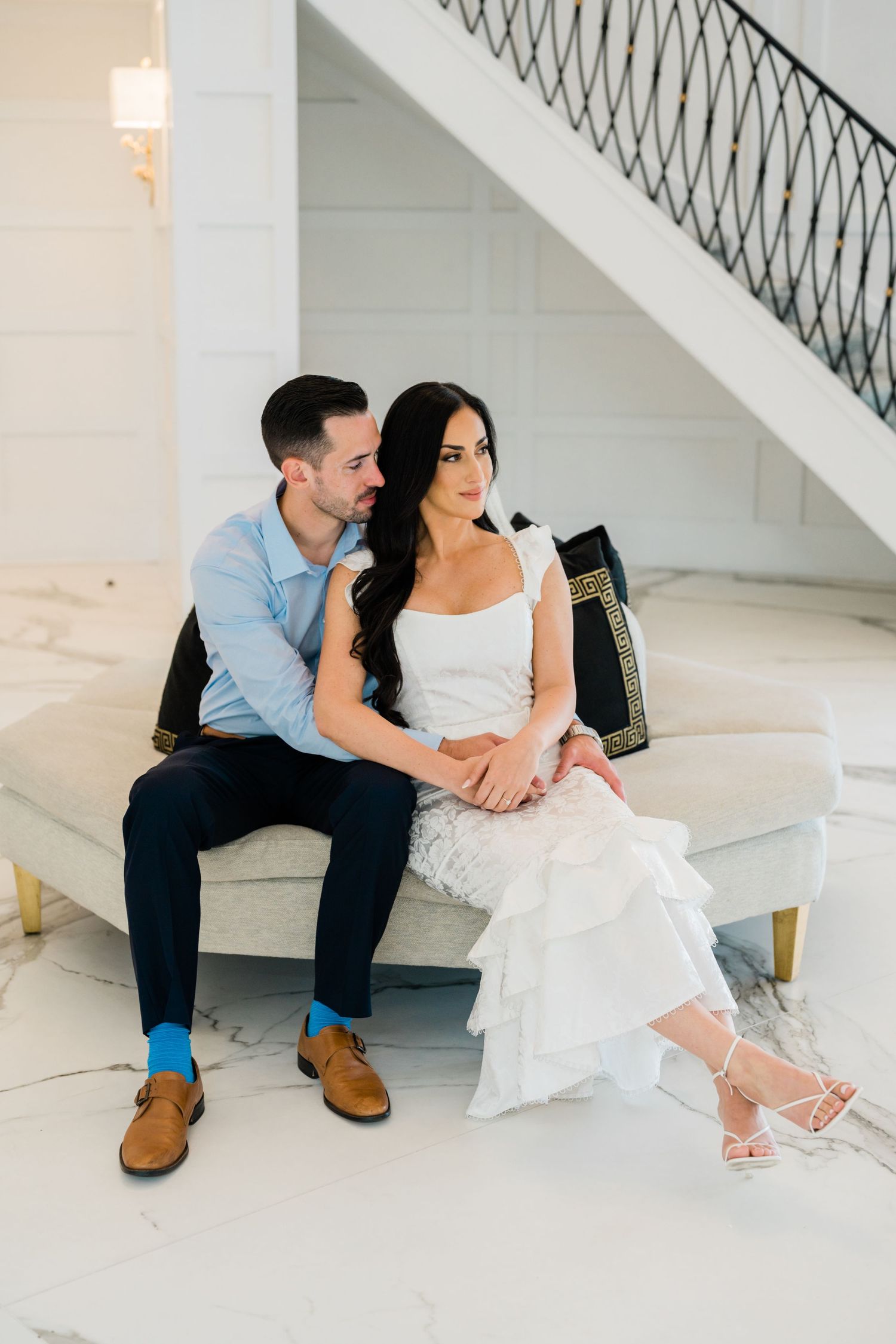 A couple sits together on white stairs sharing an intimate moment in wedding attire.