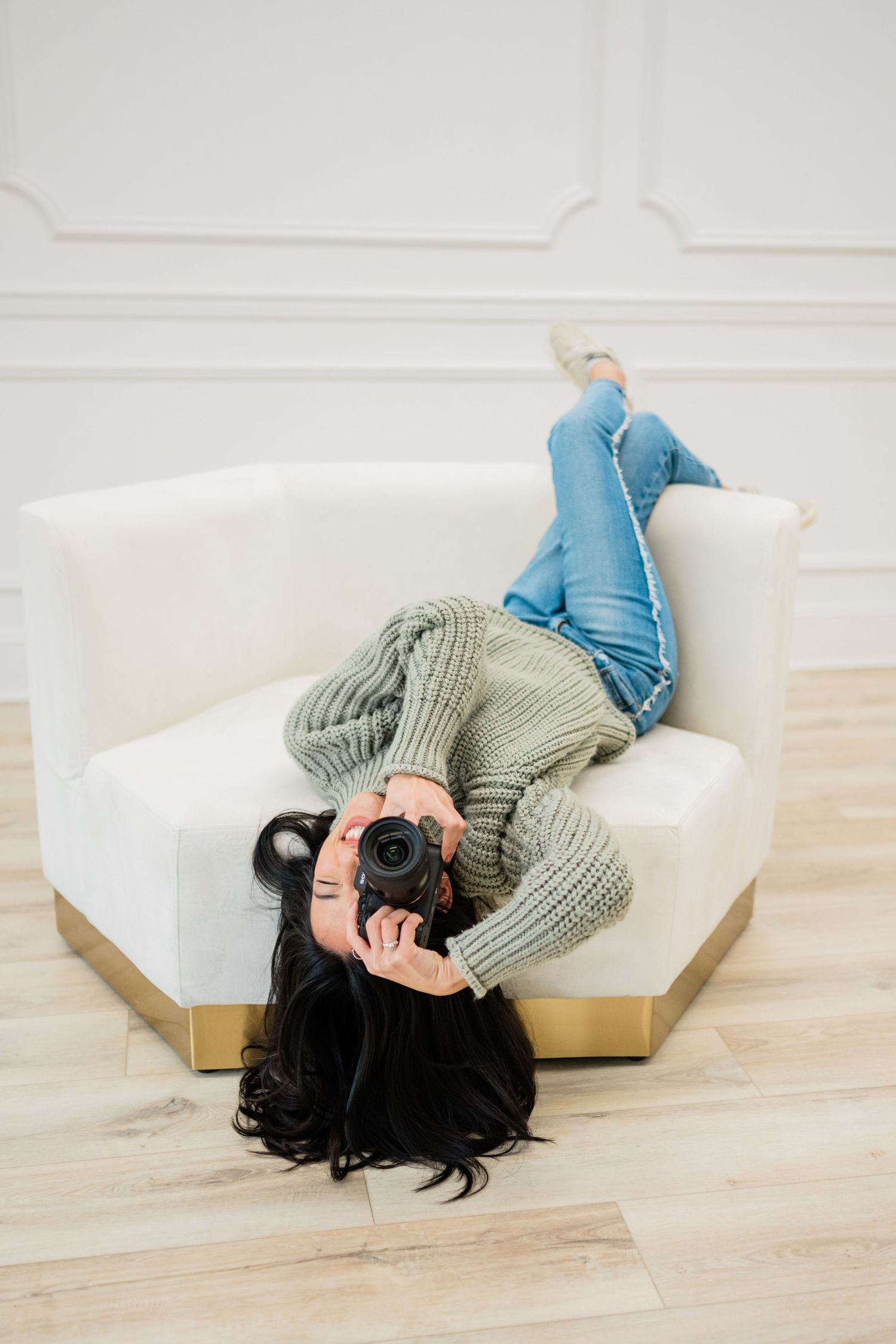 Person in gray sweater lying on white couch holding camera.