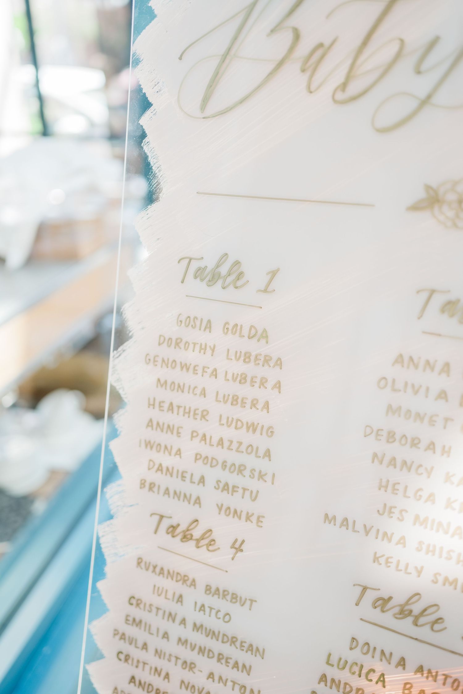 Close-up of elegant gold lettering on baby shower seating chart with guest names.