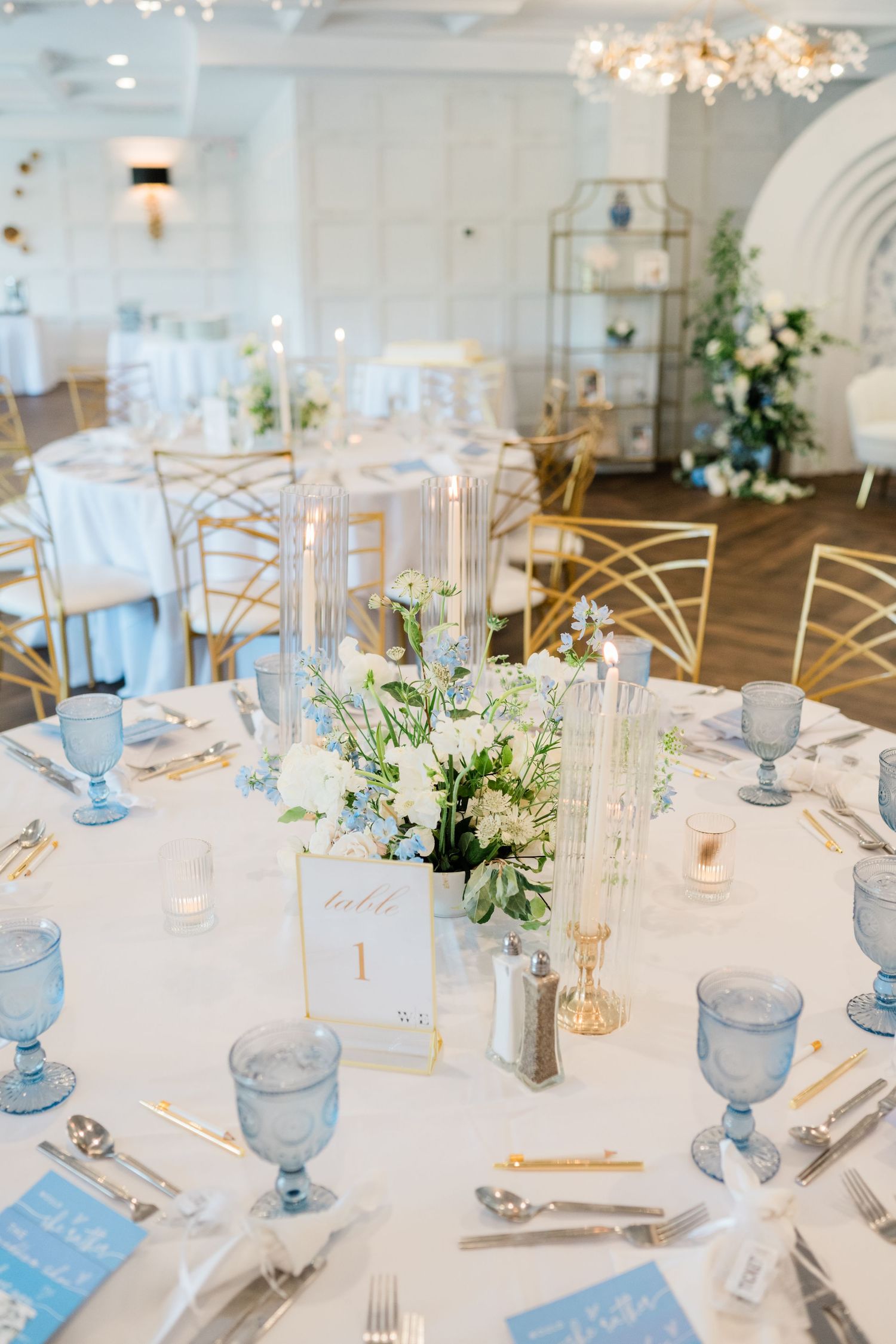 Elegant wedding reception tables set with blue glassware, white linens, and floral centerpieces.