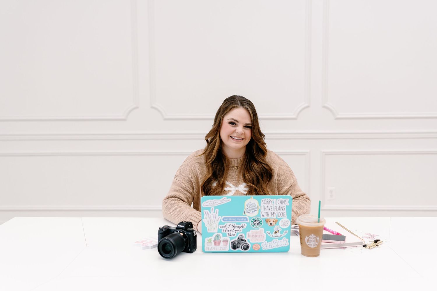 A person at a desk with a laptop, camera, and office supplies in a minimalist setting.