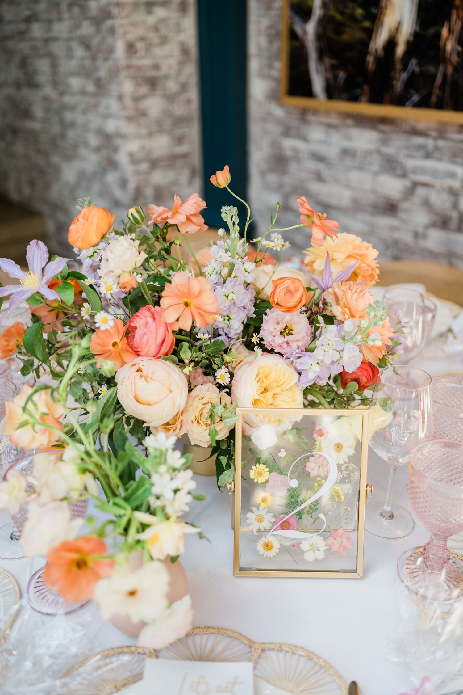 Lush floral centerpiece with peach, yellow and purple blooms in elegant table setting.