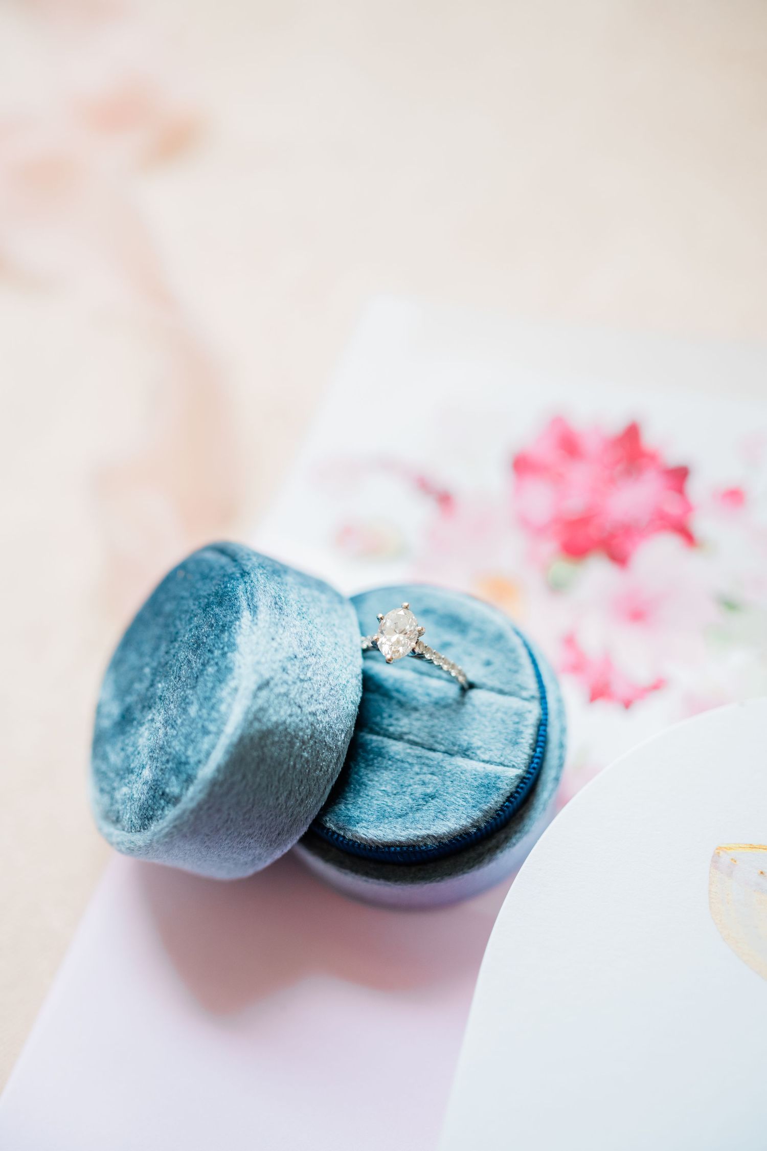 A blue velvet ring box holding an engagement ring on a light background.