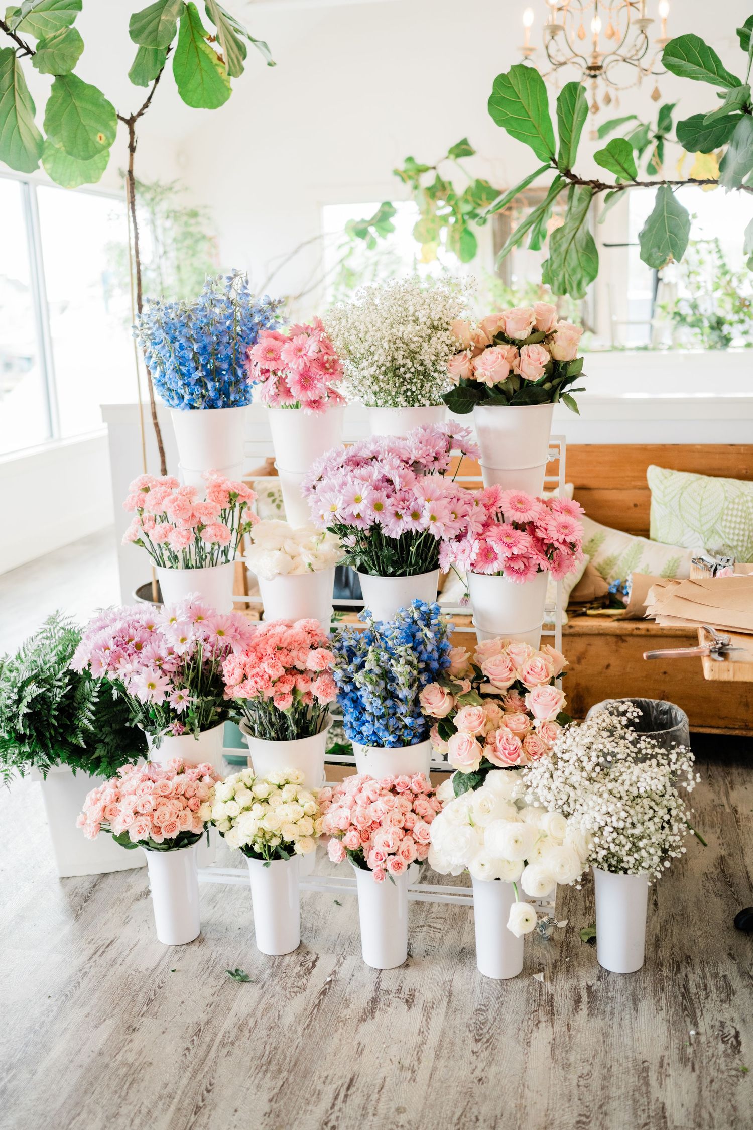 Collection of pink, white and blue flowers arranged in white vases on rustic wooden flooring.