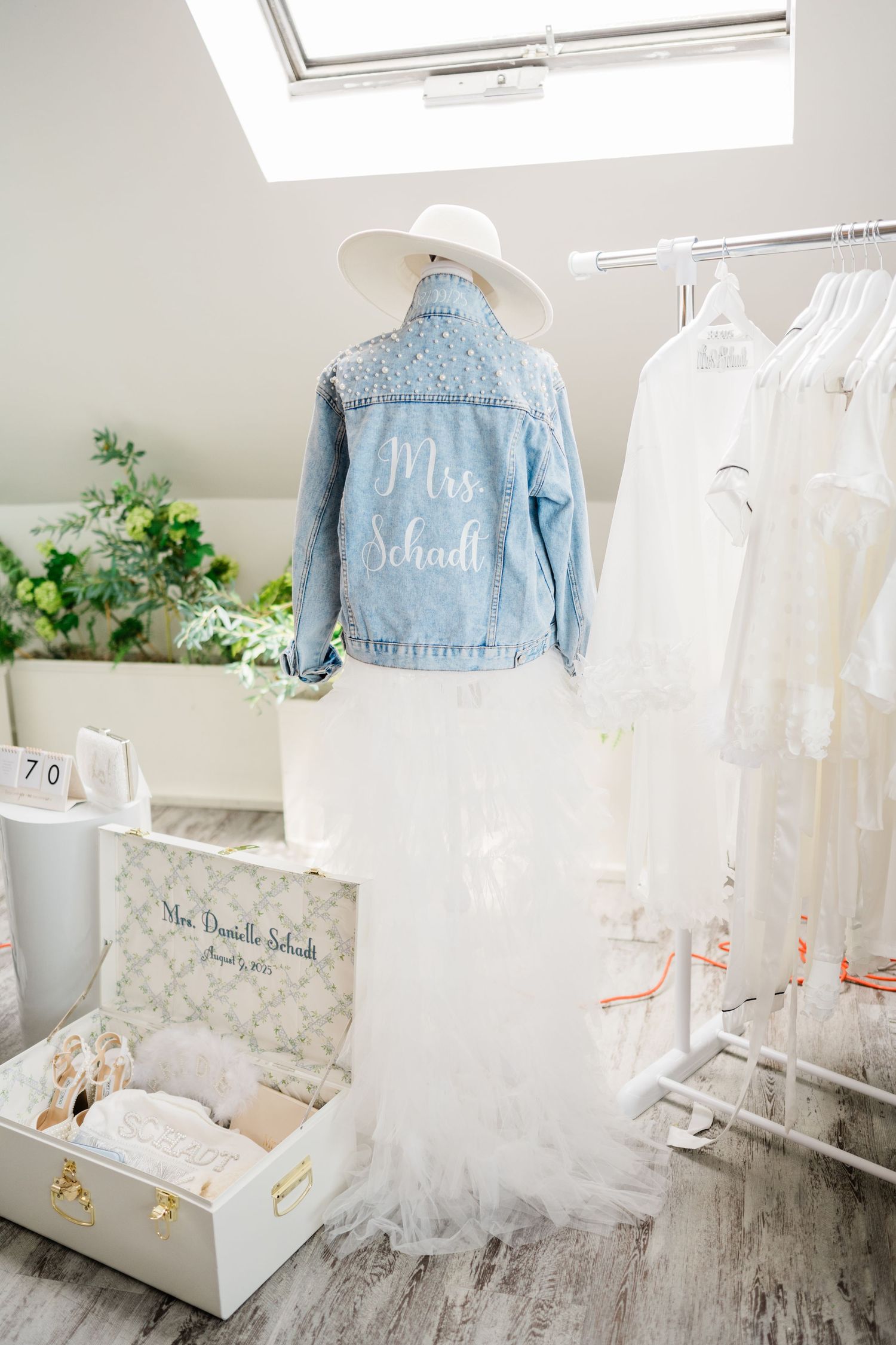 Custom denim jackets and white dresses displayed on hangers in a bright dressing room.