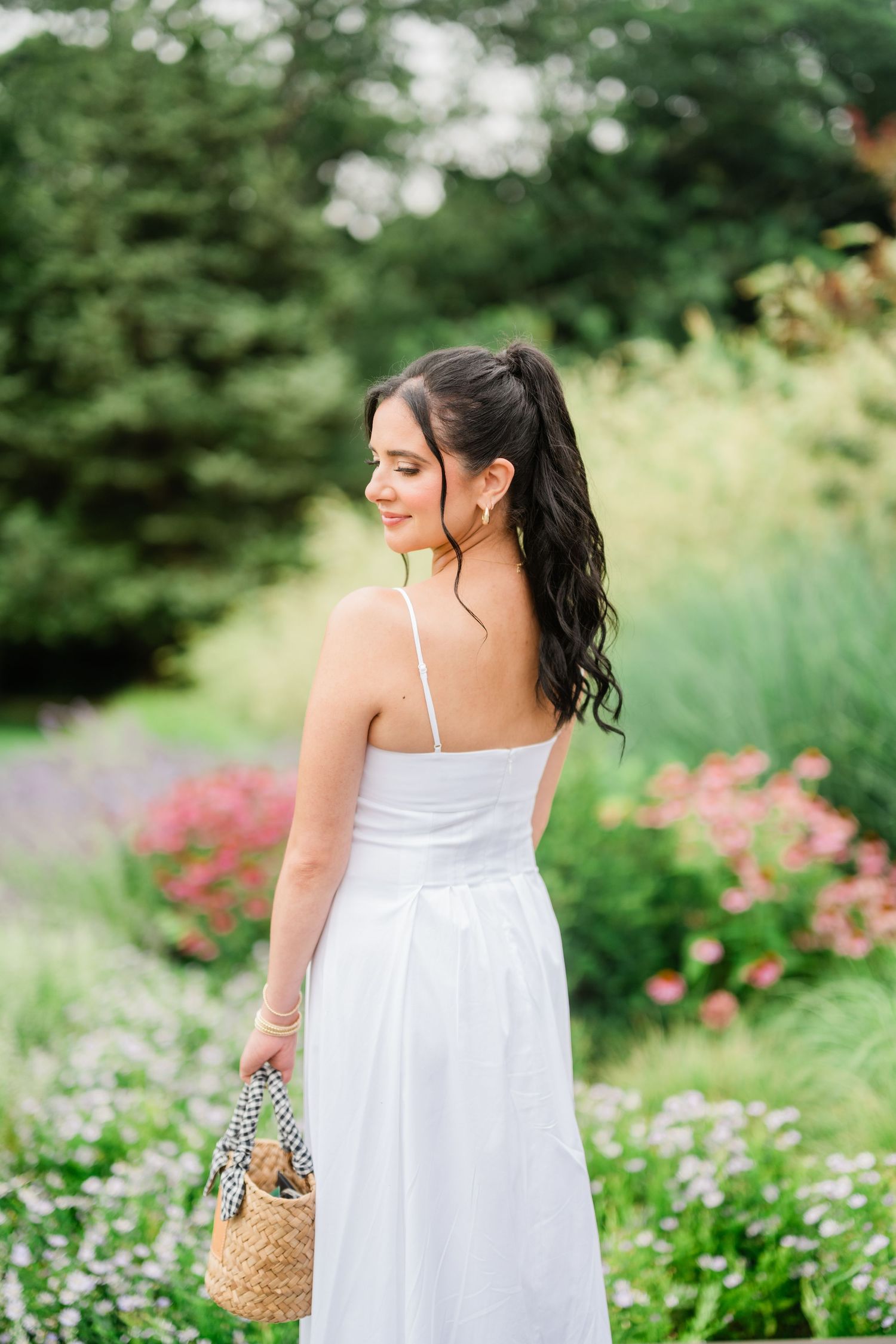 Woman in white sundress walking through a garden with blooming flowers.