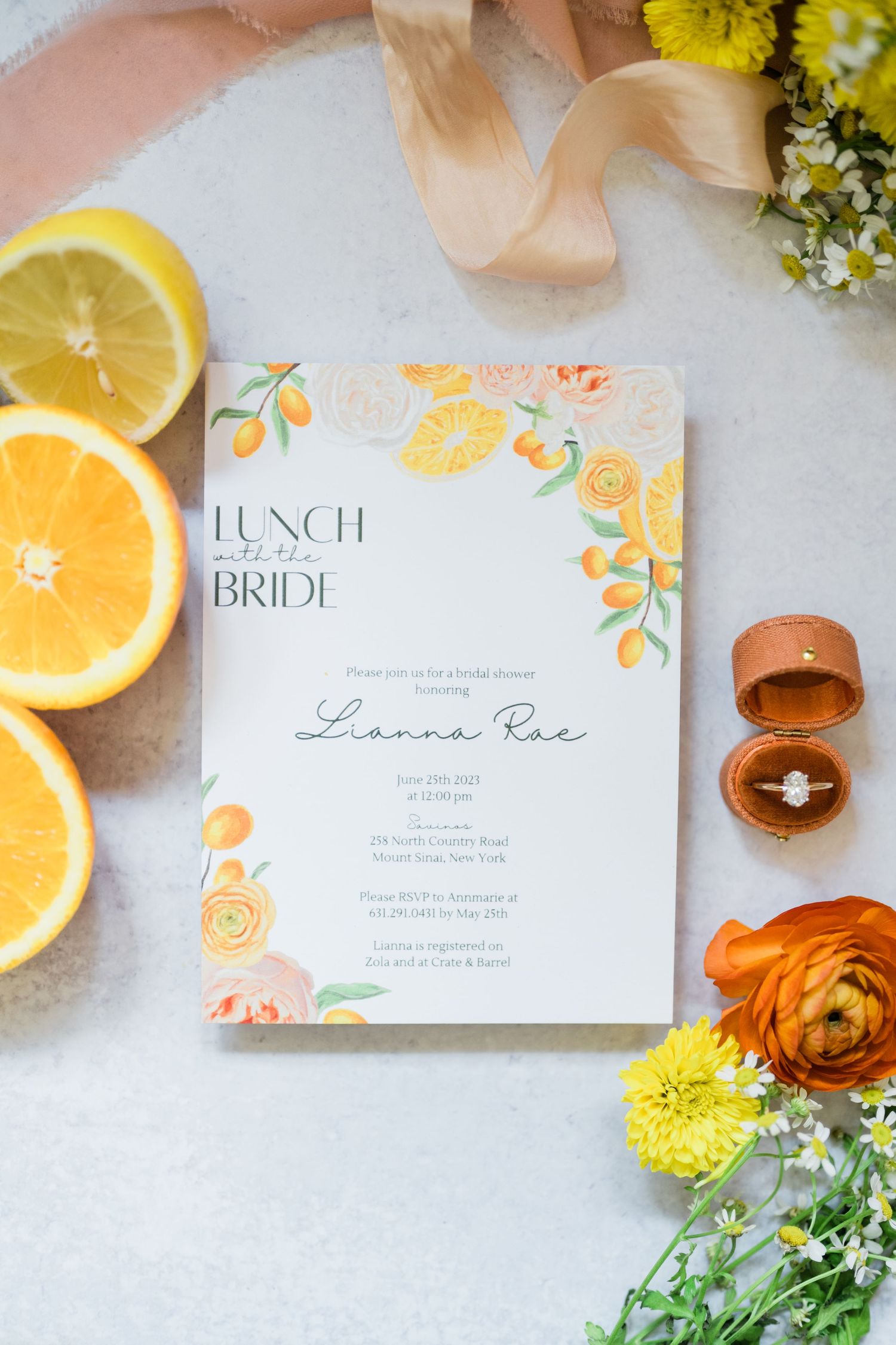 Bridal lunch invitation with citrus design elements and ring box on white surface.