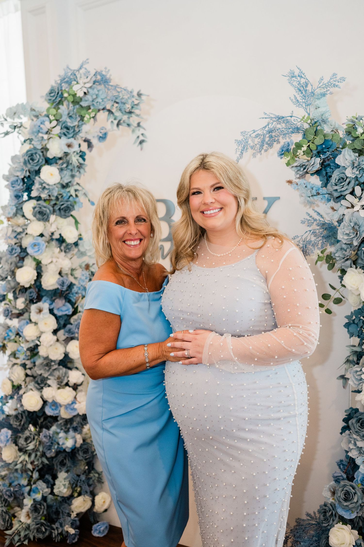 Two guests posing together in front of elegant blue and white floral backdrop.
