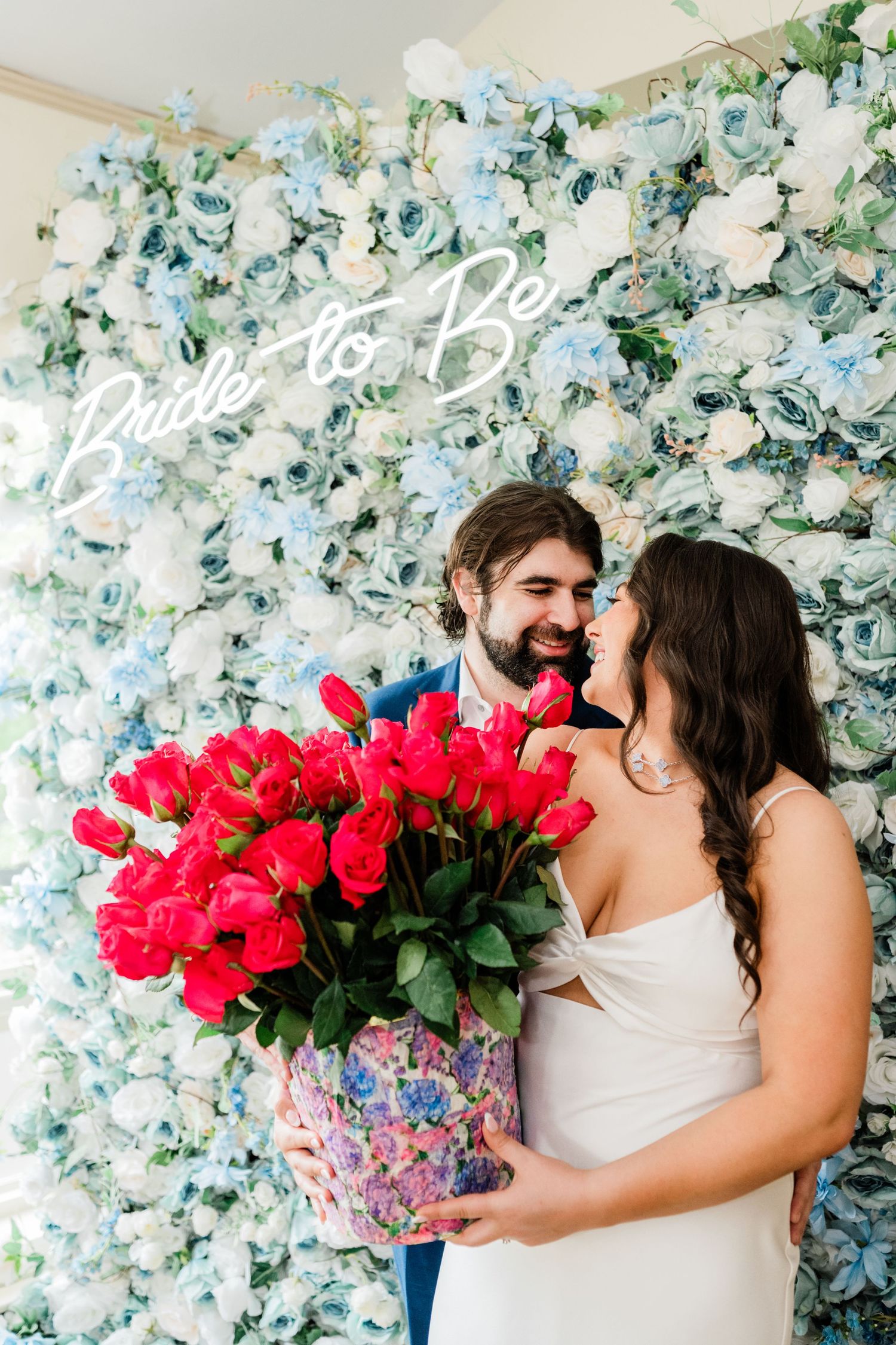 A romantic moment against a floral backdrop with vibrant red roses and blue hydrangeas.