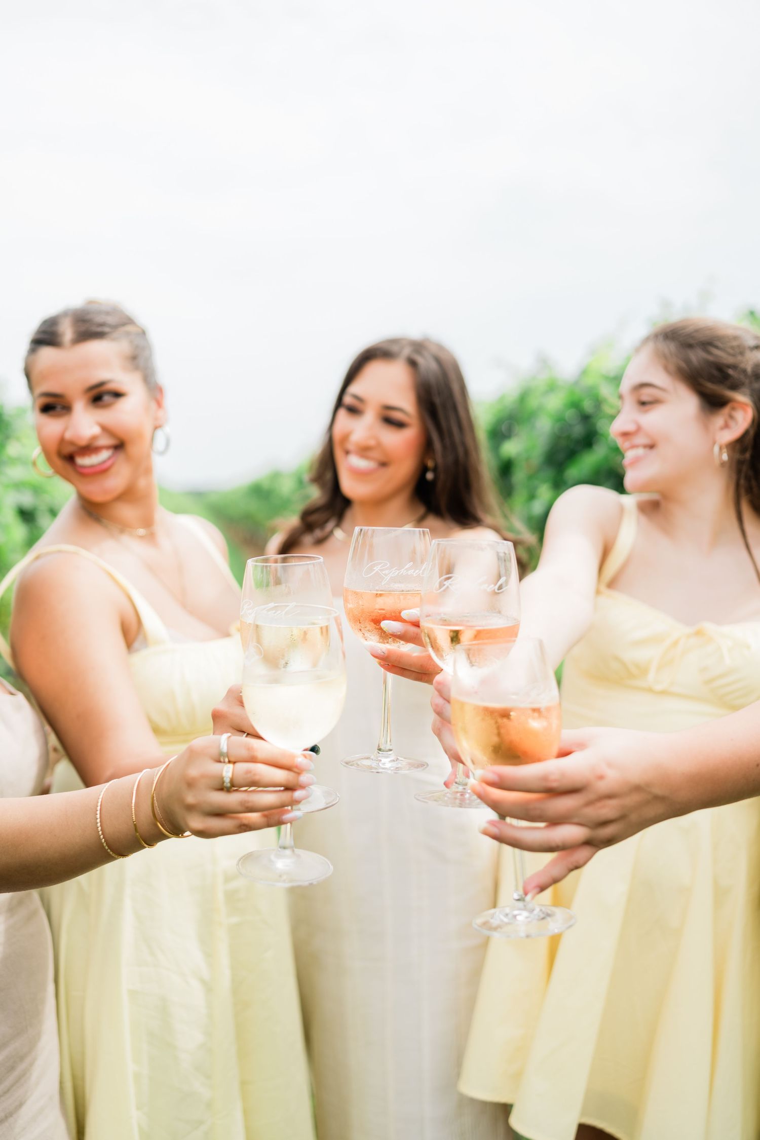 Bridesmaids in pale yellow dresses toast with champagne glasses at an outdoor wedding celebration.