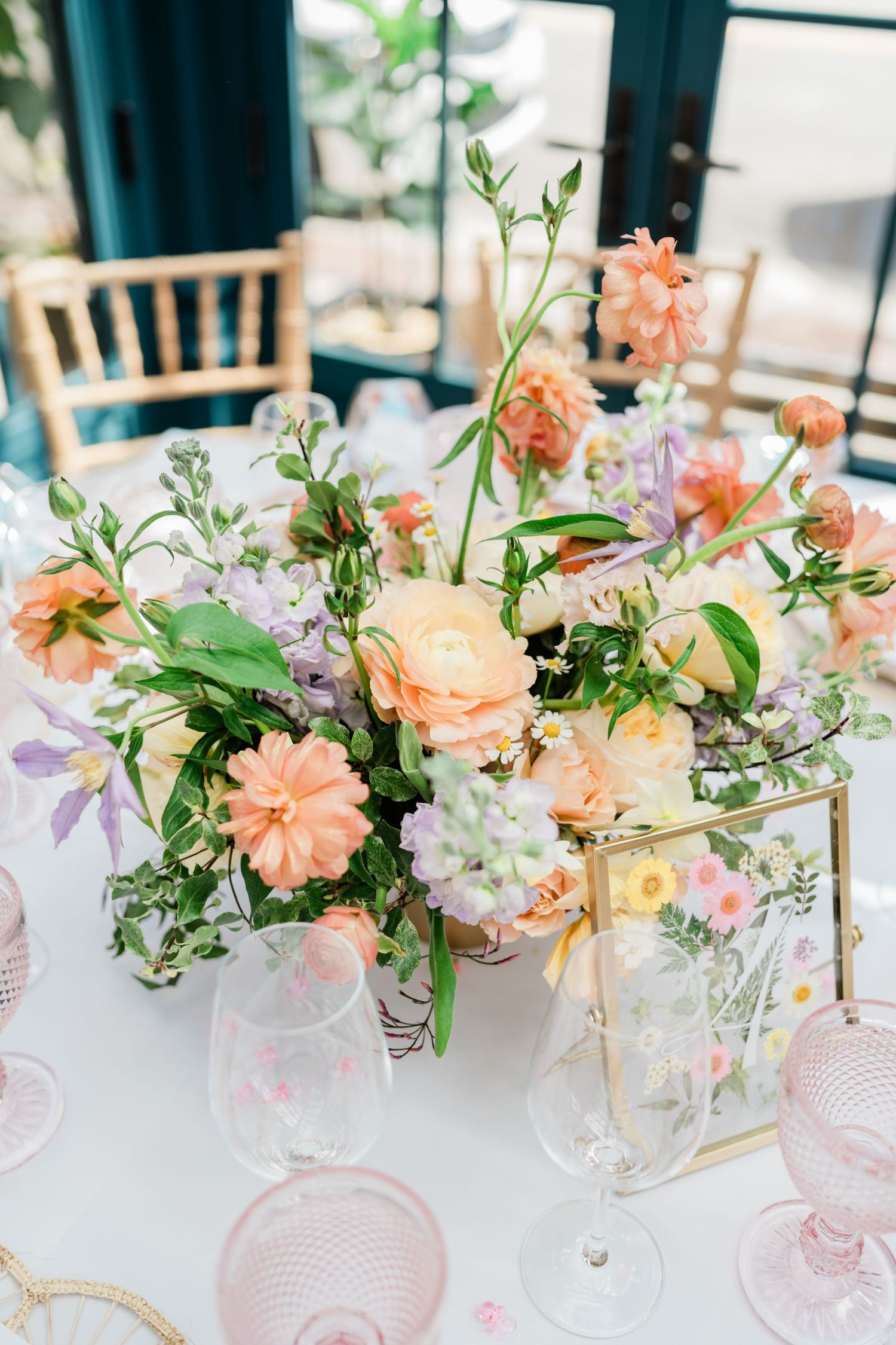 Elegant peach and white floral centerpiece with roses and greenery in a gold-framed glass vase on a wedding table setting.