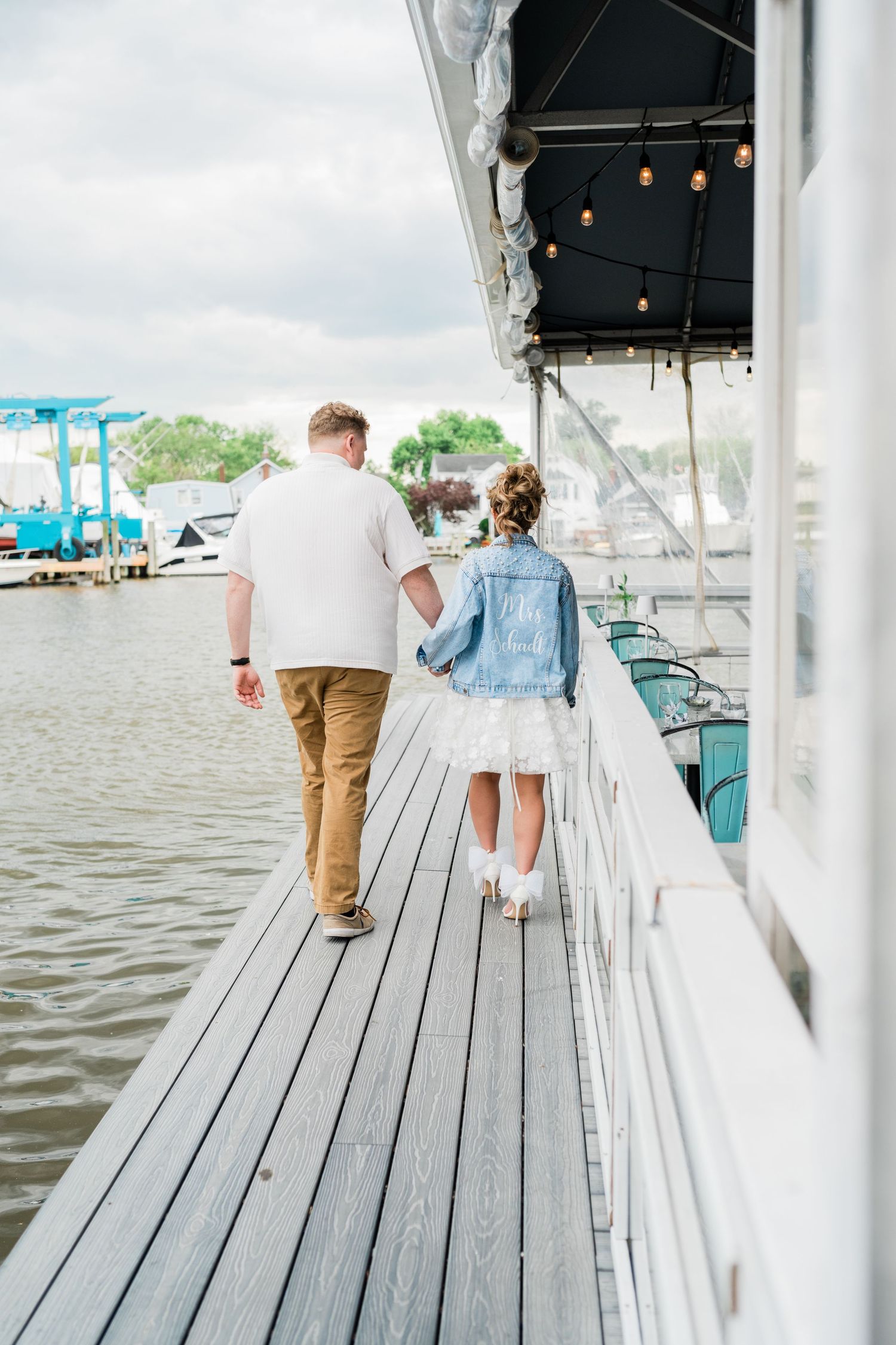 A couple strolls along a waterfront wooden deck with cloudy skies in the background.