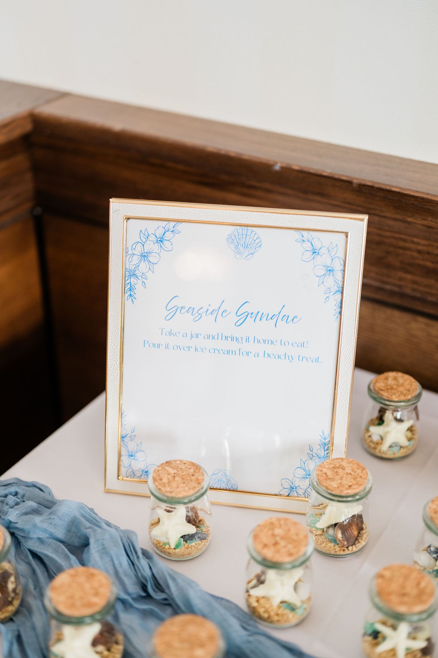 Decorative seaside-themed sign with blue text and ornate border on wooden surface.