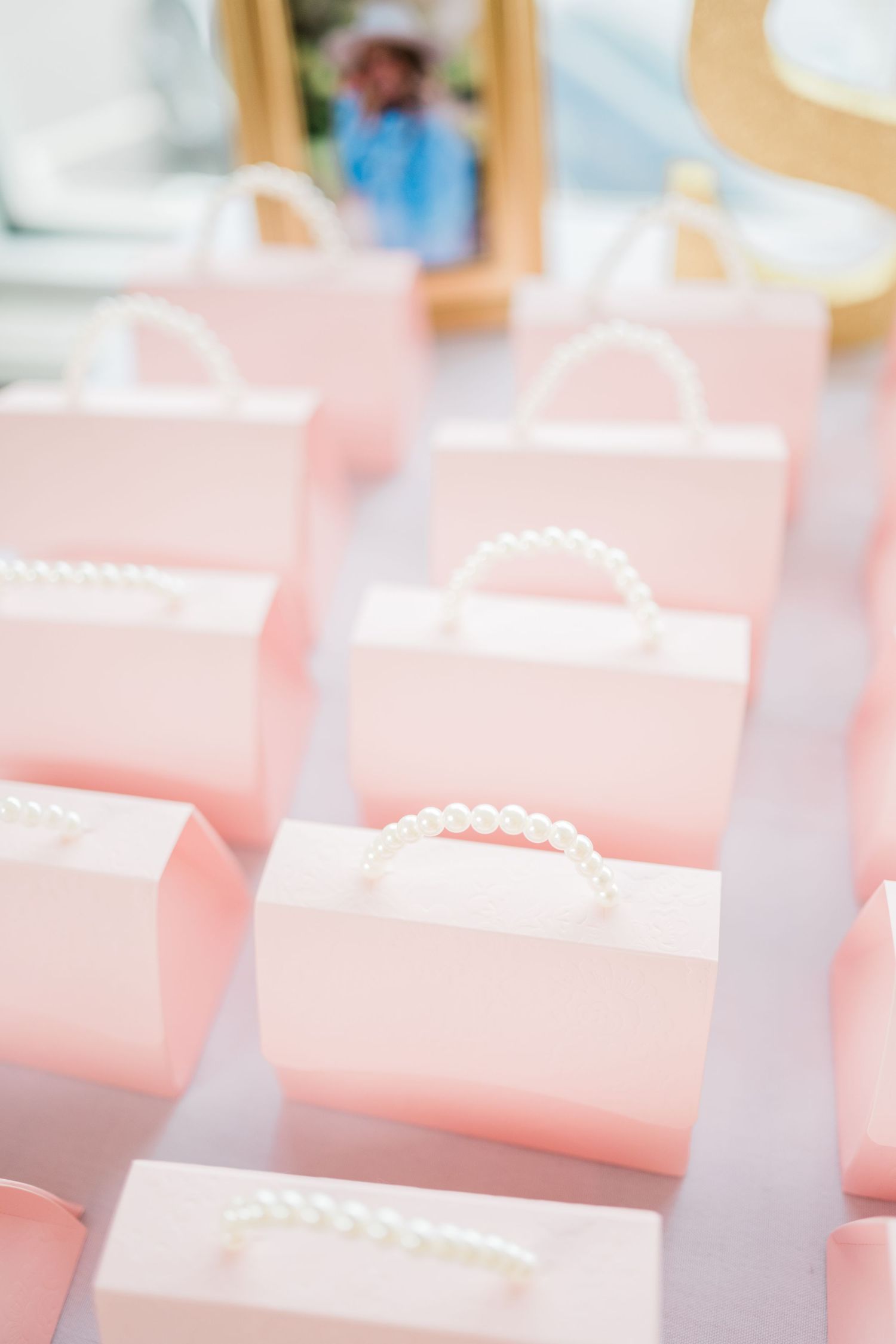 Row of soft pink gift bags with pearl handles arranged neatly on a table.