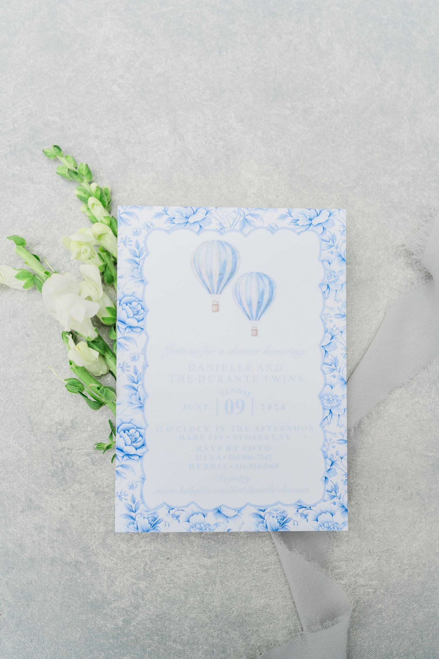 Baby shower invitation with delicate blue hot air balloon design and floral border.