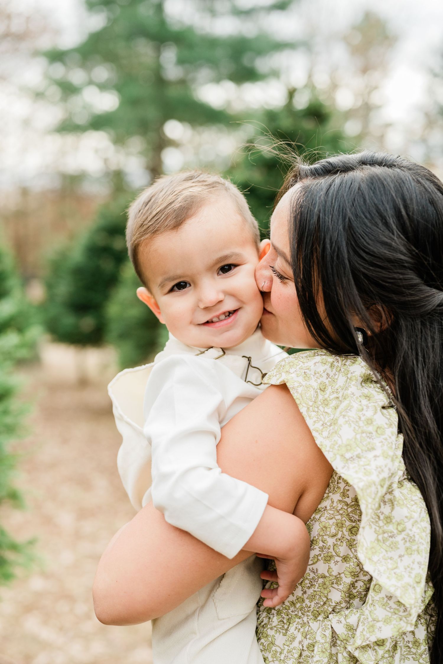 Sweet moment captured outdoors with parent giving child a kiss against natural forest backdrop.