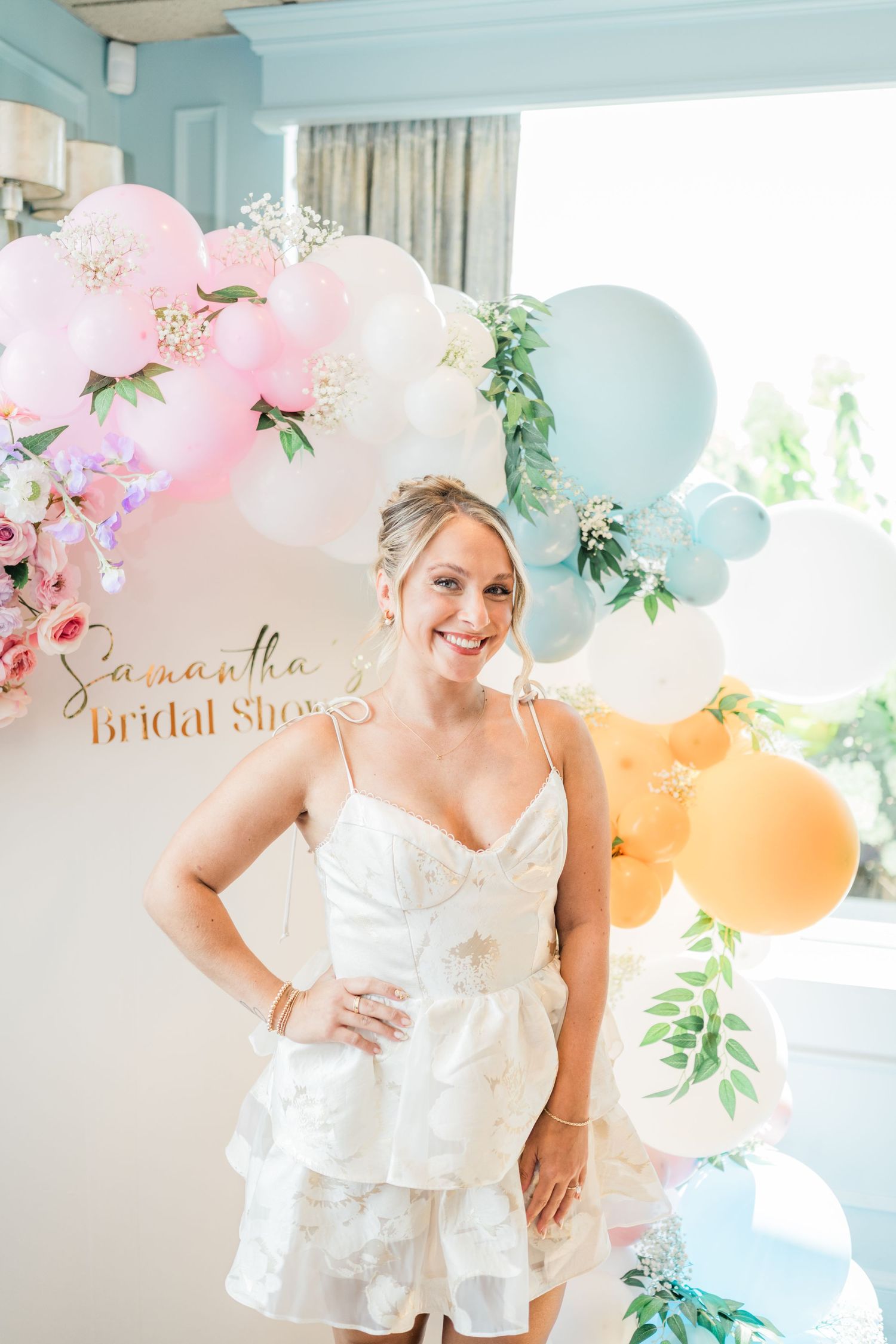Bridal shower celebration with pink and blue balloons, floral decorations, and white lace dress details.