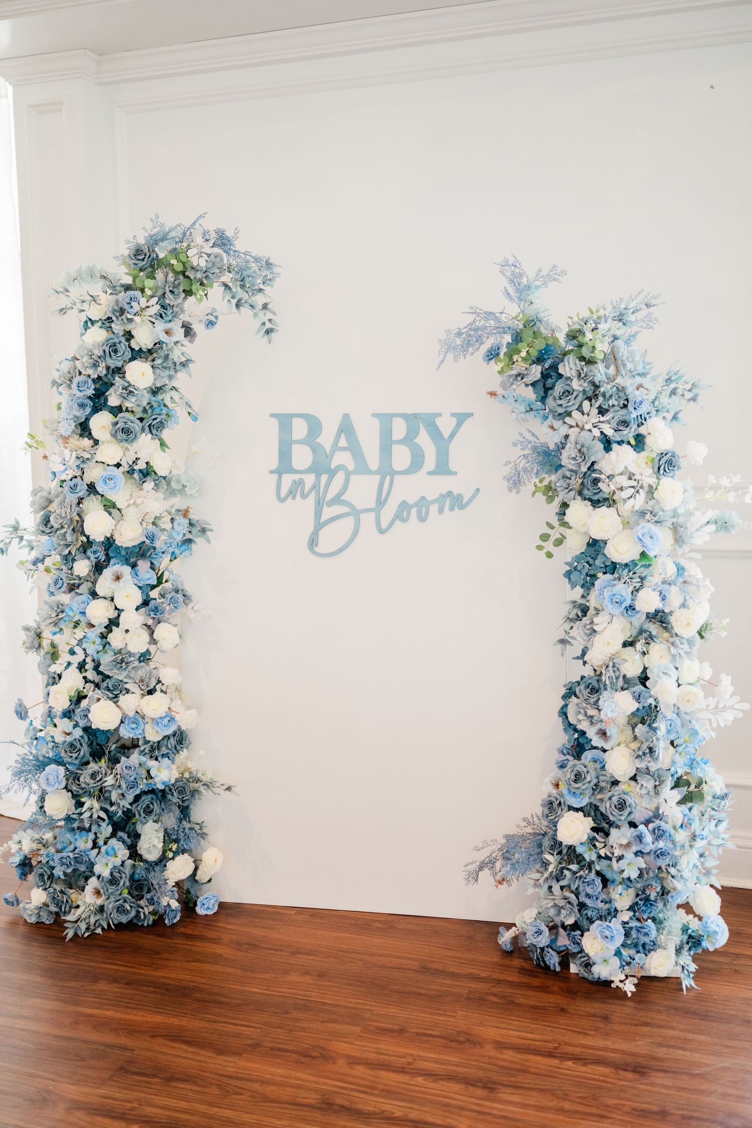 Blue and white floral arrangements flanking baby shower signage on white wall.