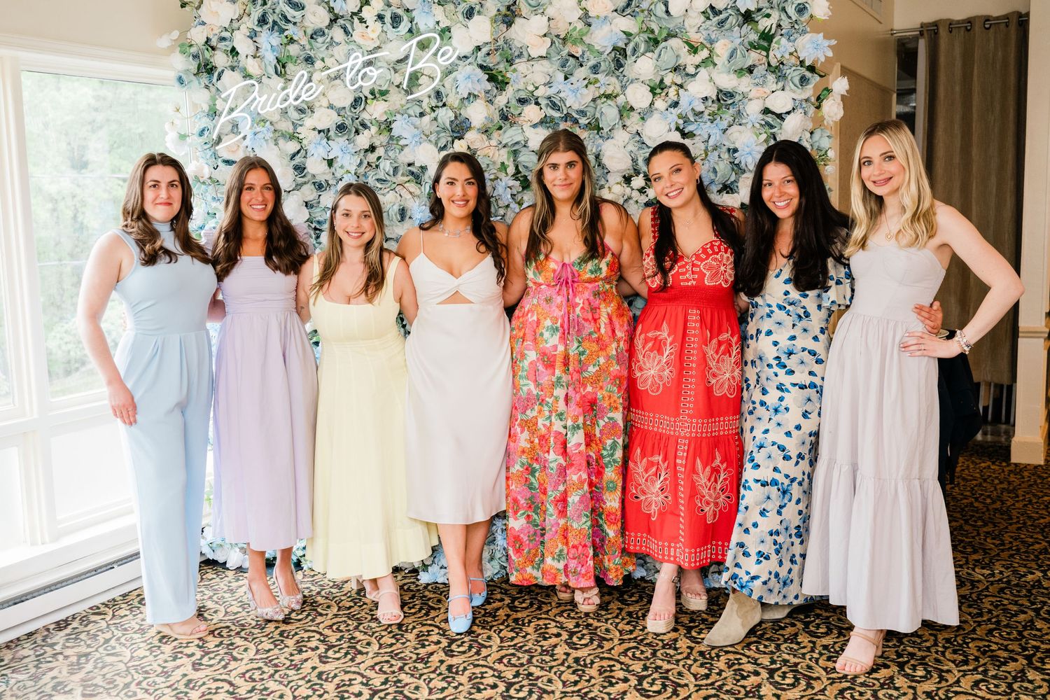 Bridesmaids in pastel dresses and coral floral prints pose together at a wedding venue.