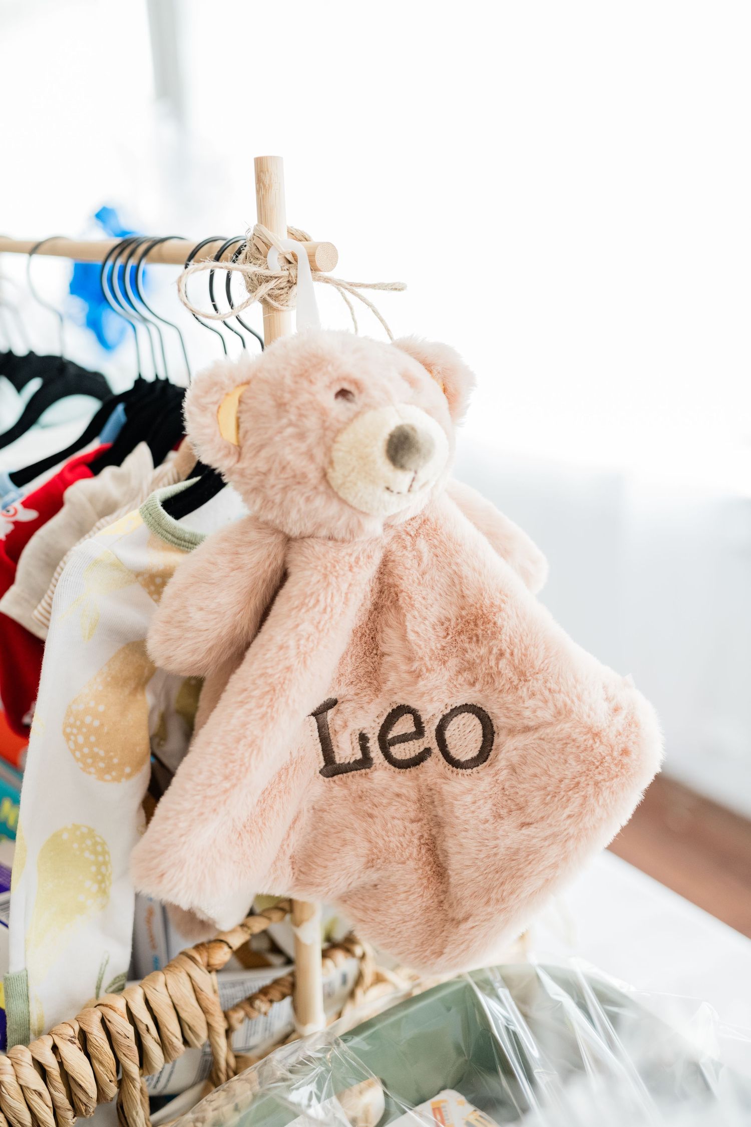Pink plush baby clothing item with 'Leo' text displayed on a clothing rack.