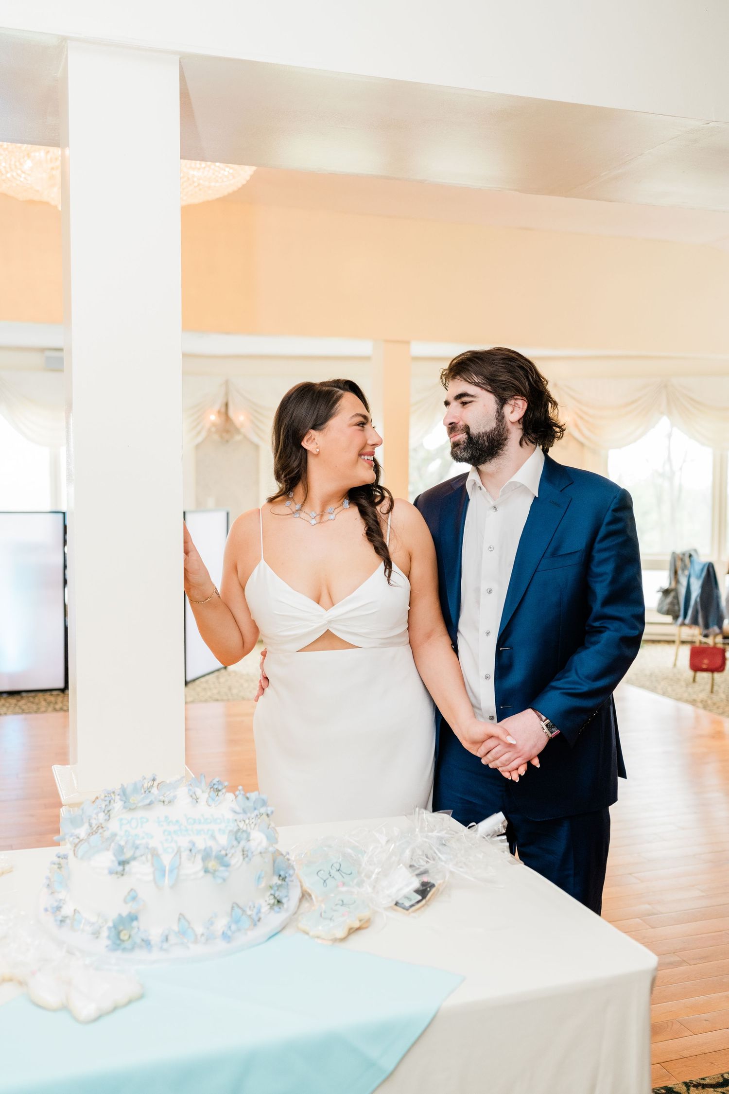 A couple shares a joyful moment in a bright indoor venue with blue floral decorations.