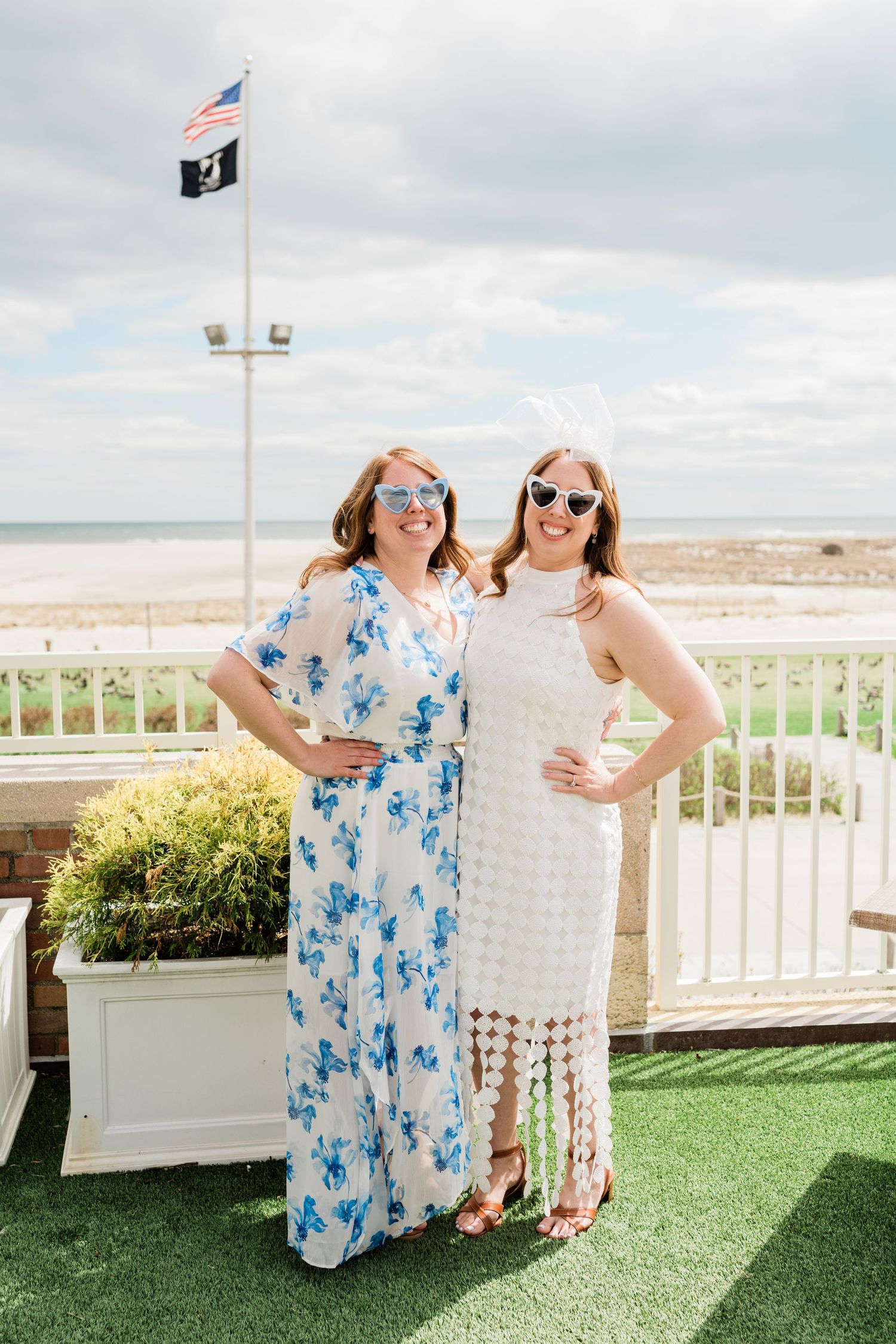 Two people posing on an outdoor deck with white railing and ocean view.
