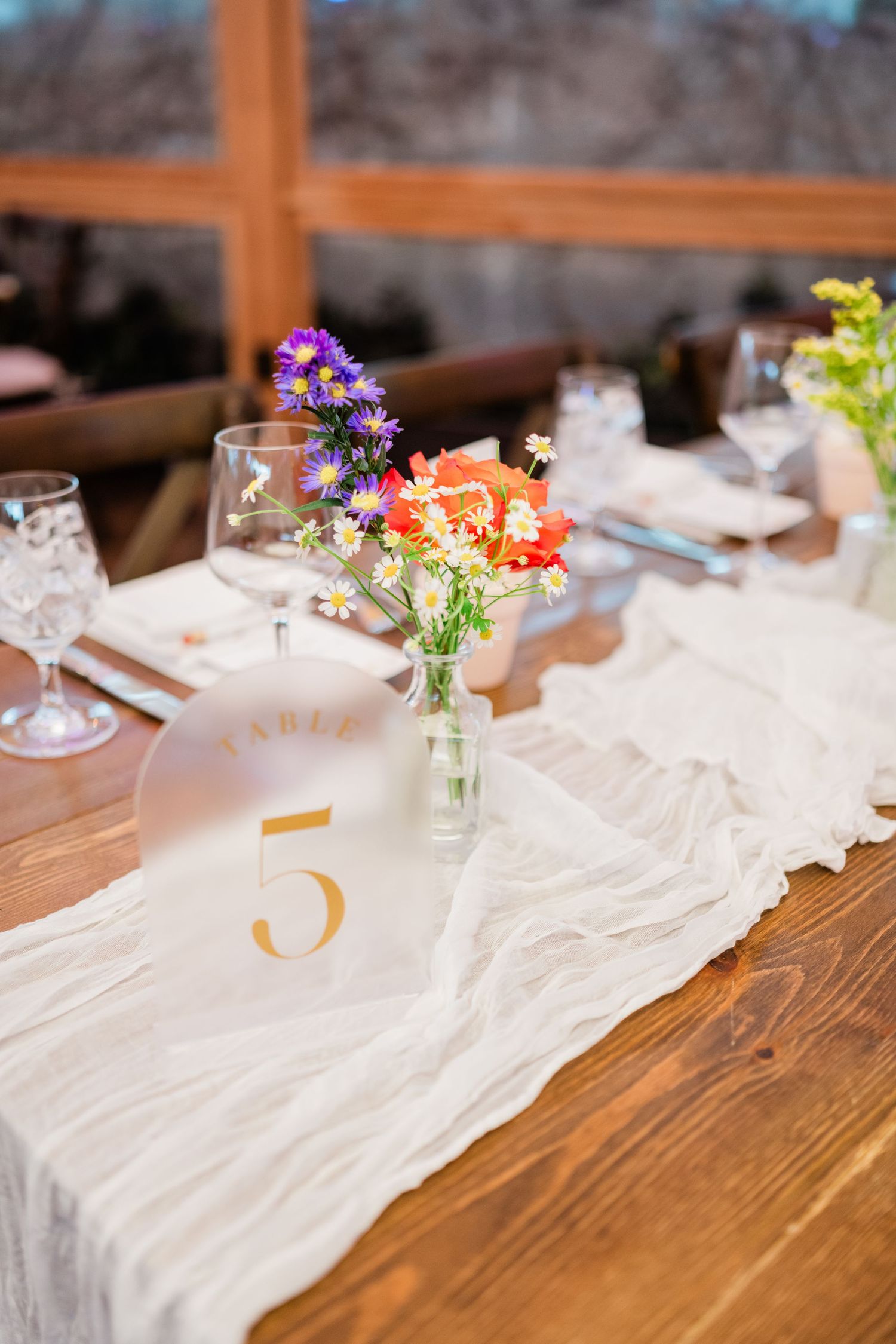 Rustic wooden table decorated with small vases of colorful wildflowers and white table linens.