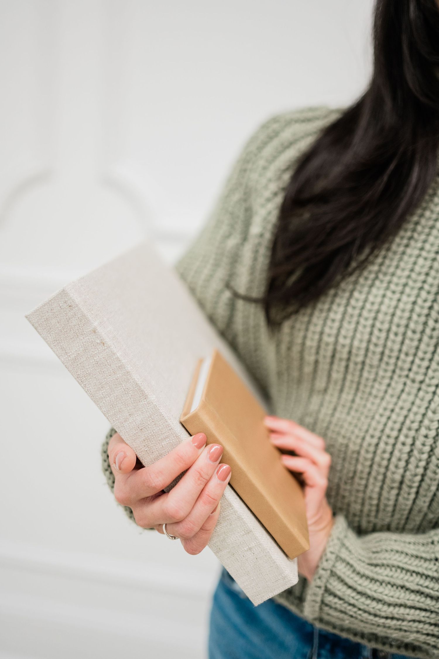 Close-up of hands holding product packaging in sage green sweater.