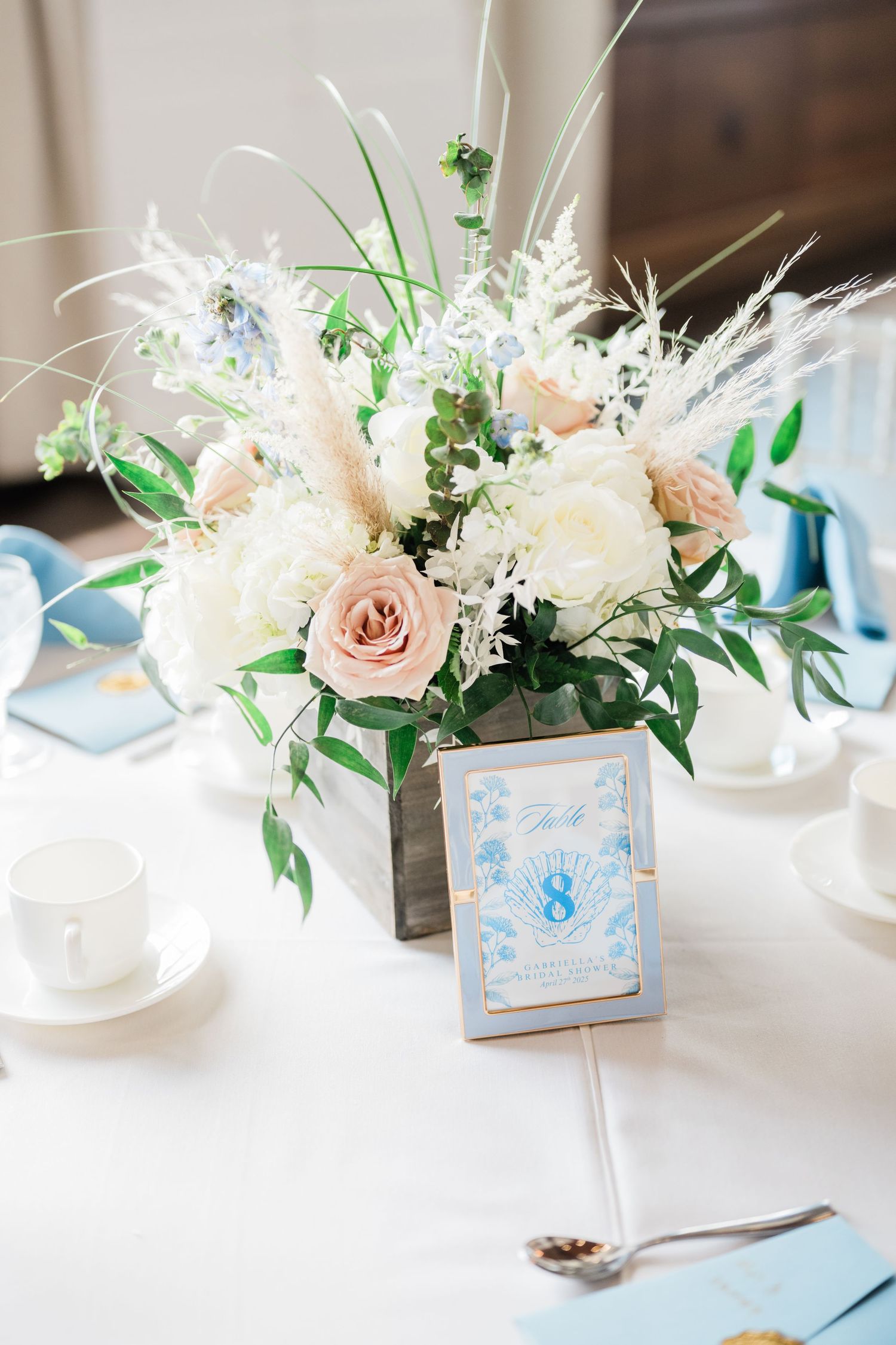 Elegant floral centerpieces with white and blush roses paired with delicate blue place cards.