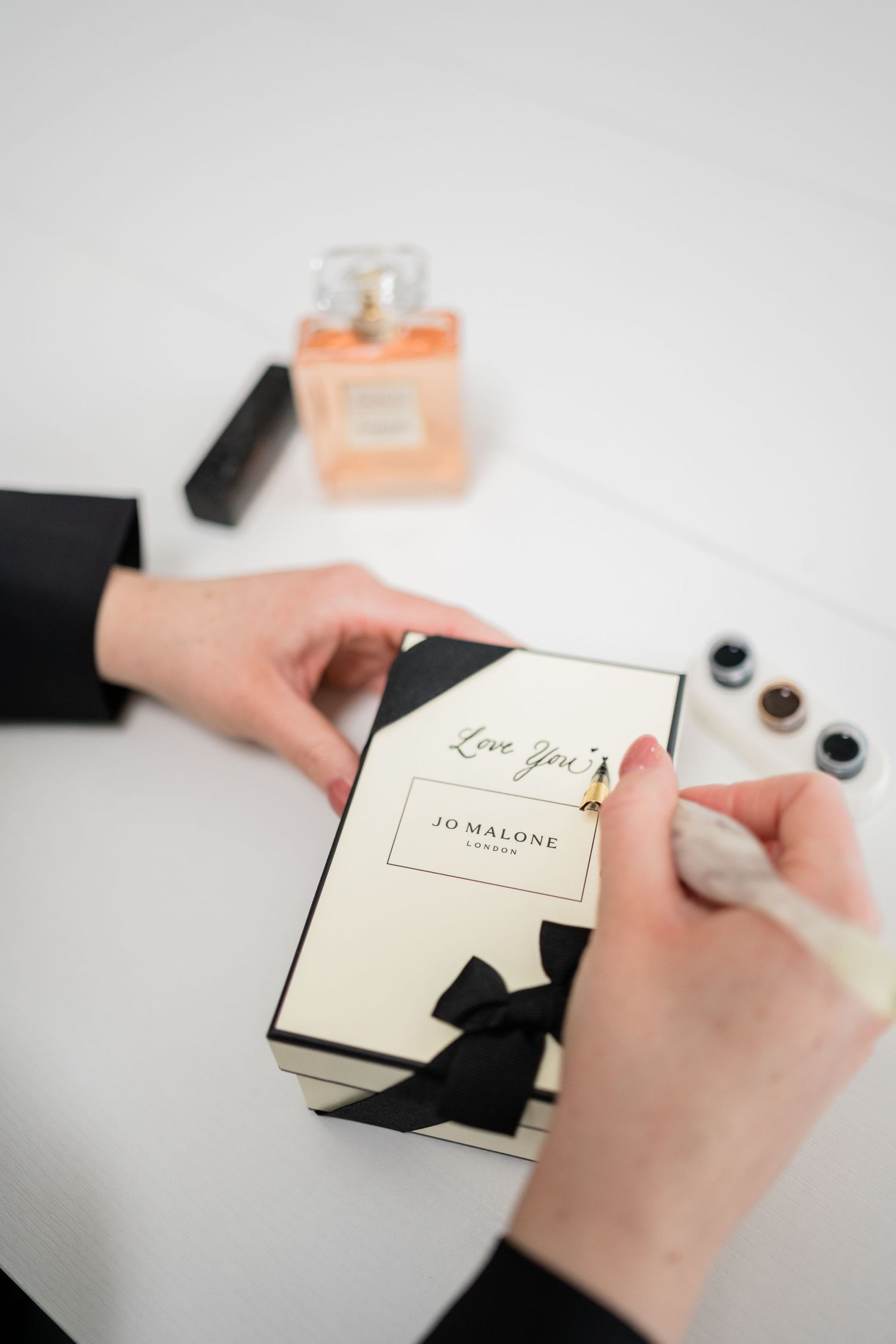 Hands writing in an elegant journal with black ink on a white surface.