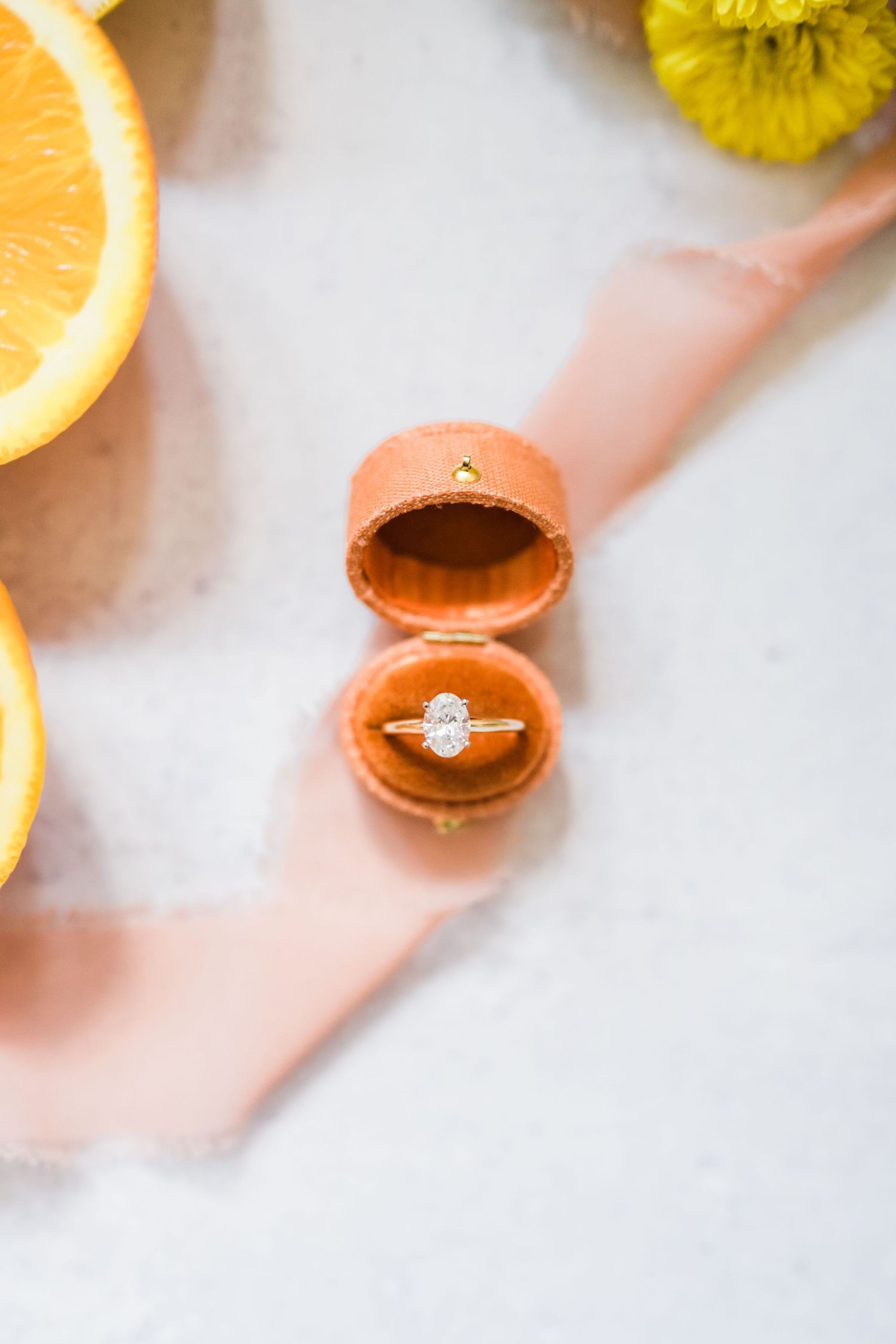 Diamond engagement ring in coral velvet ring box with orange slices.