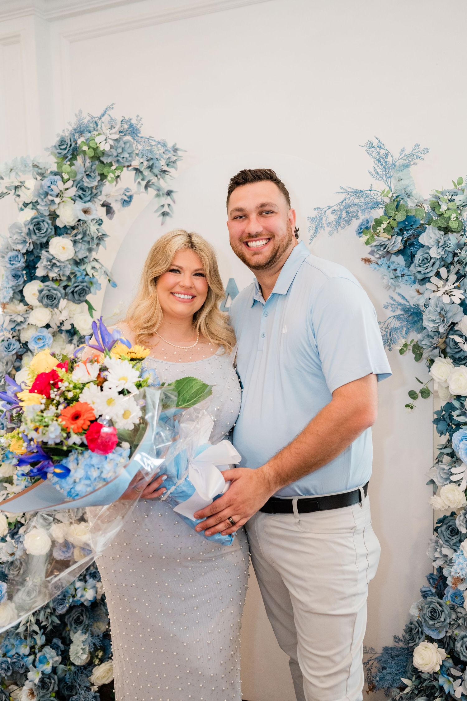 Couple posing in front of blue and white floral arch at baby shower celebration.