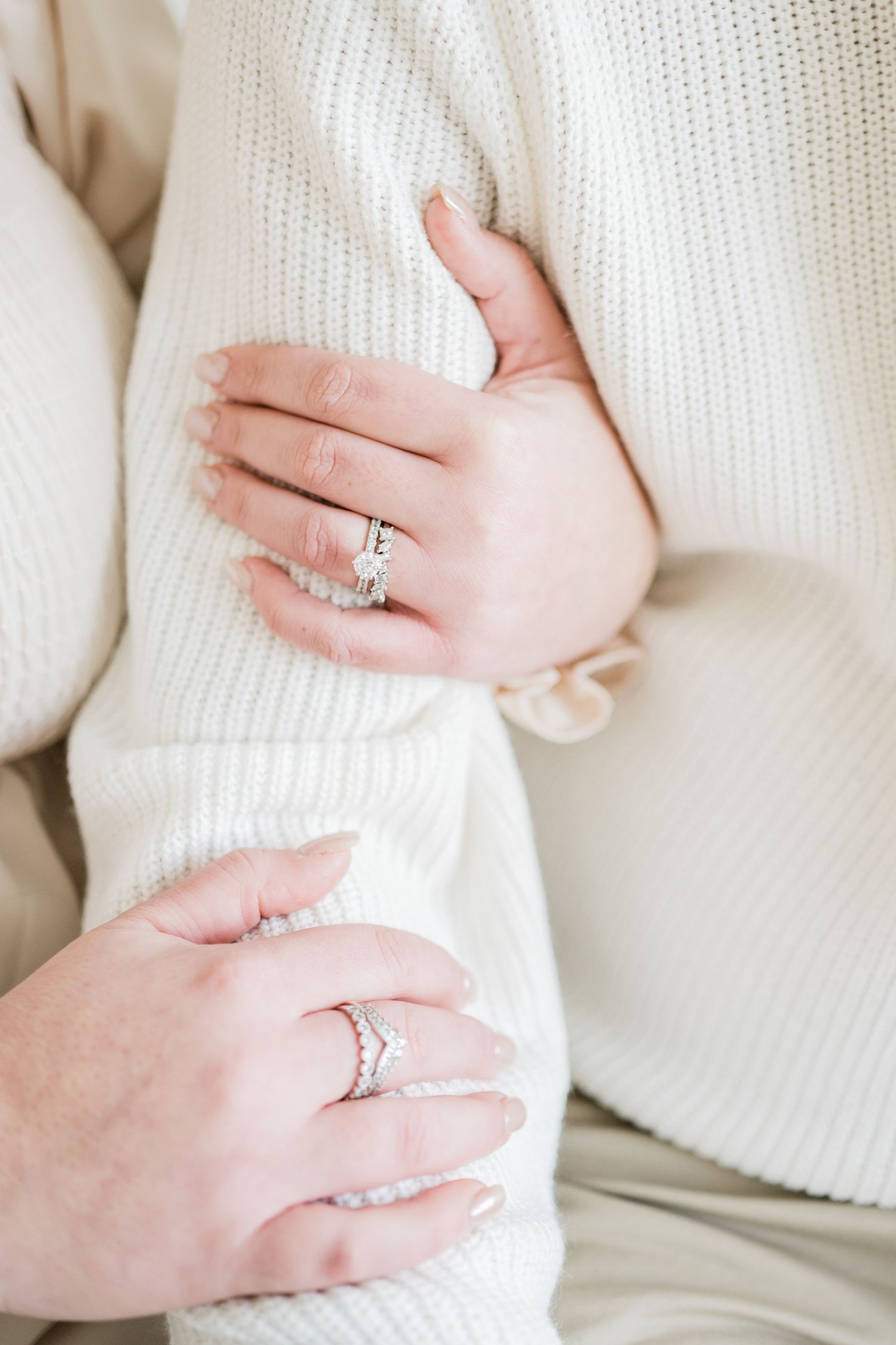 Close up of hands with engagement rings against white knit sweater background.