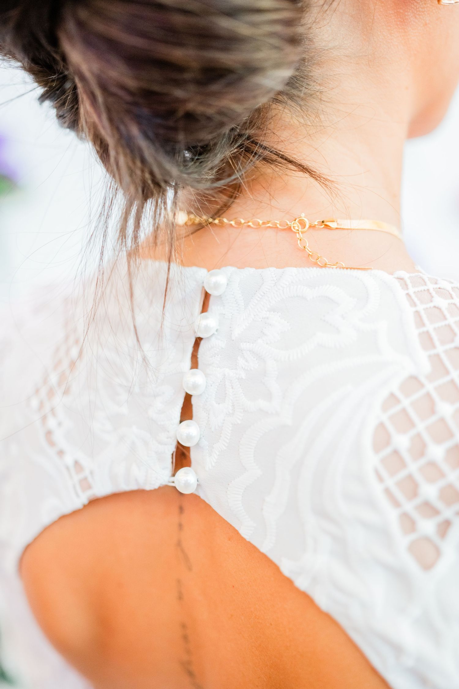 Close-up of a delicate white lace dress detail with crisscross pattern and gold necklace.