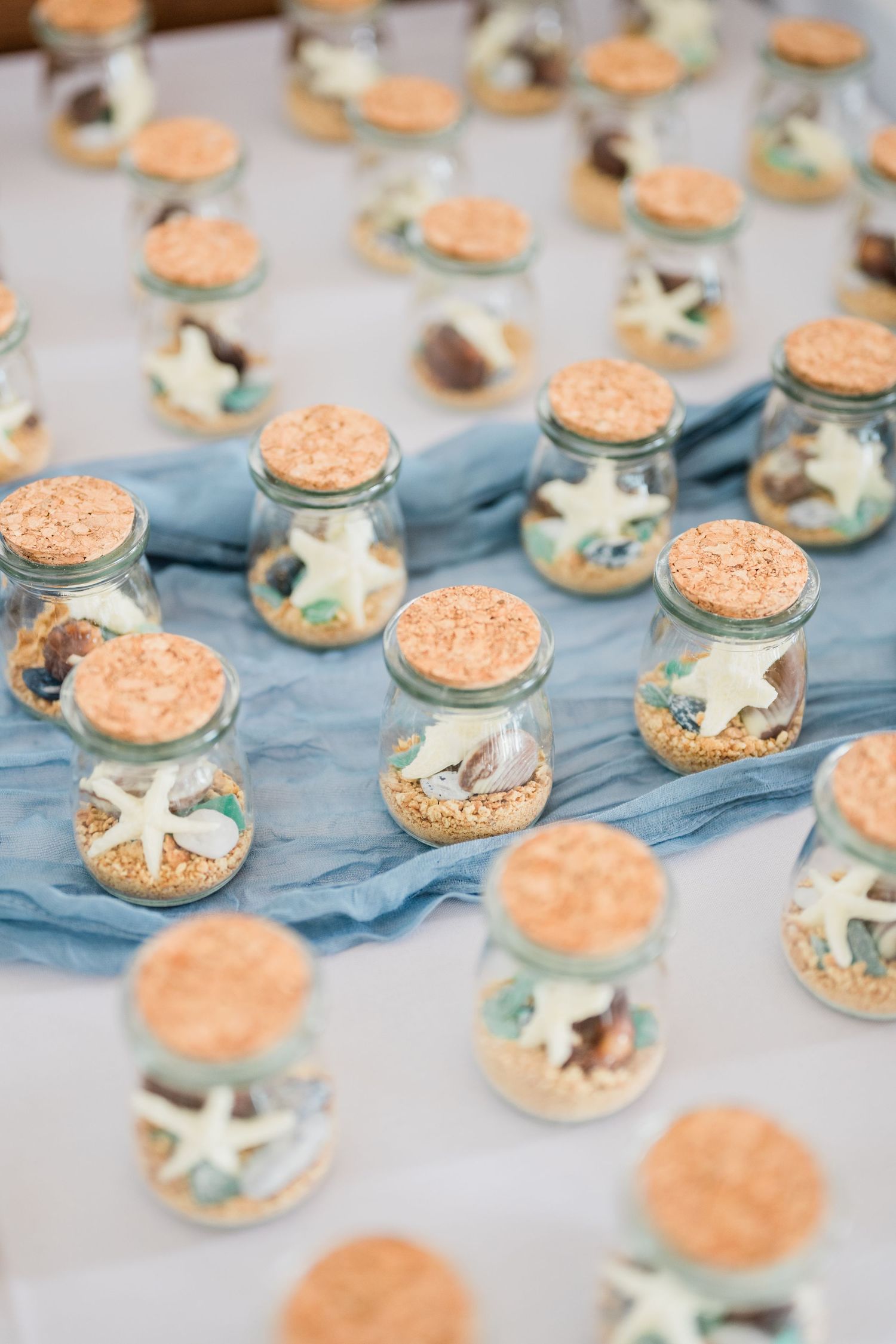 Beach-themed party favors featuring small jars with seashells and coral-colored lids.